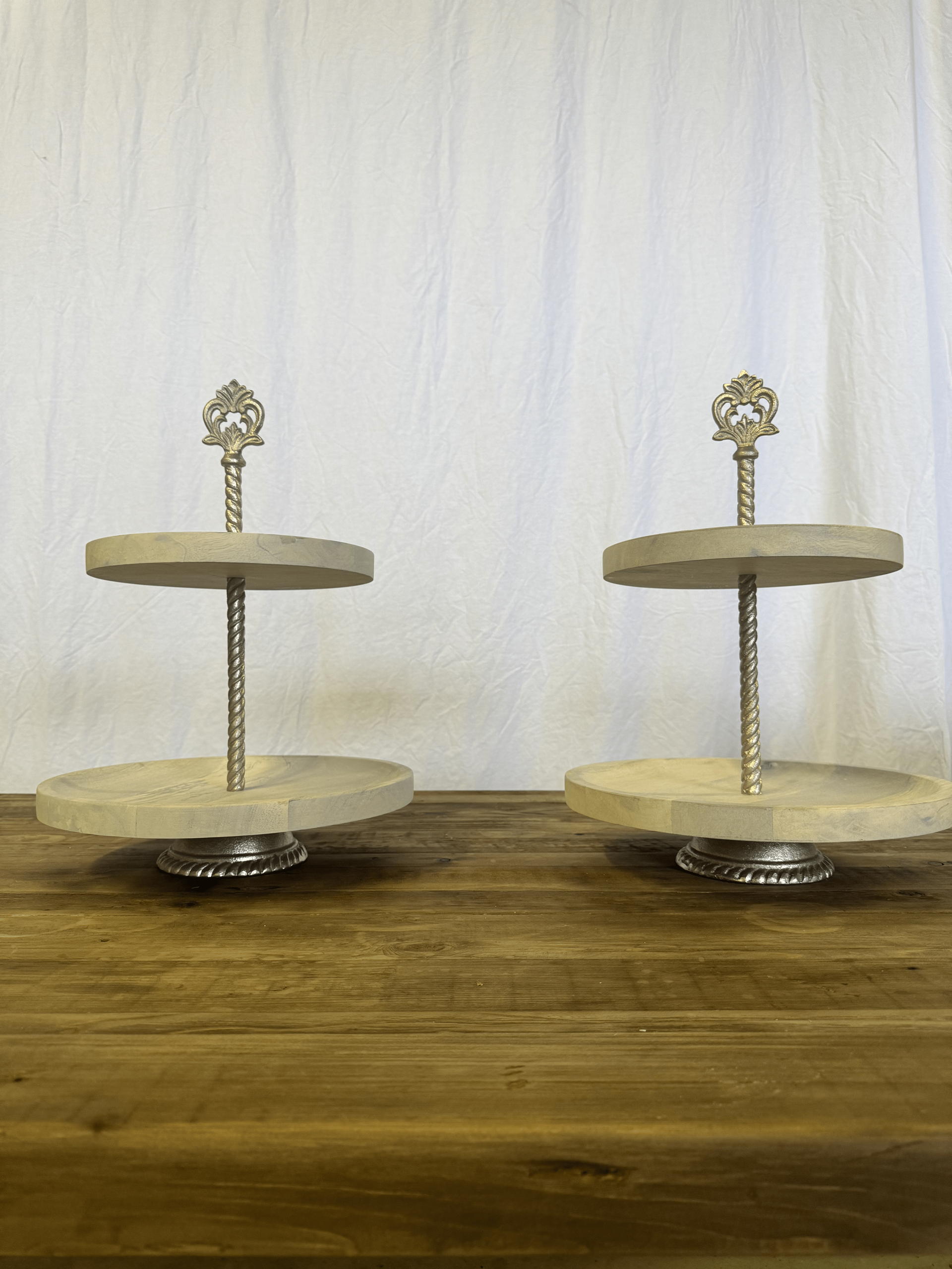 Two-tier silver dessert stands on a wooden table against a white backdrop
