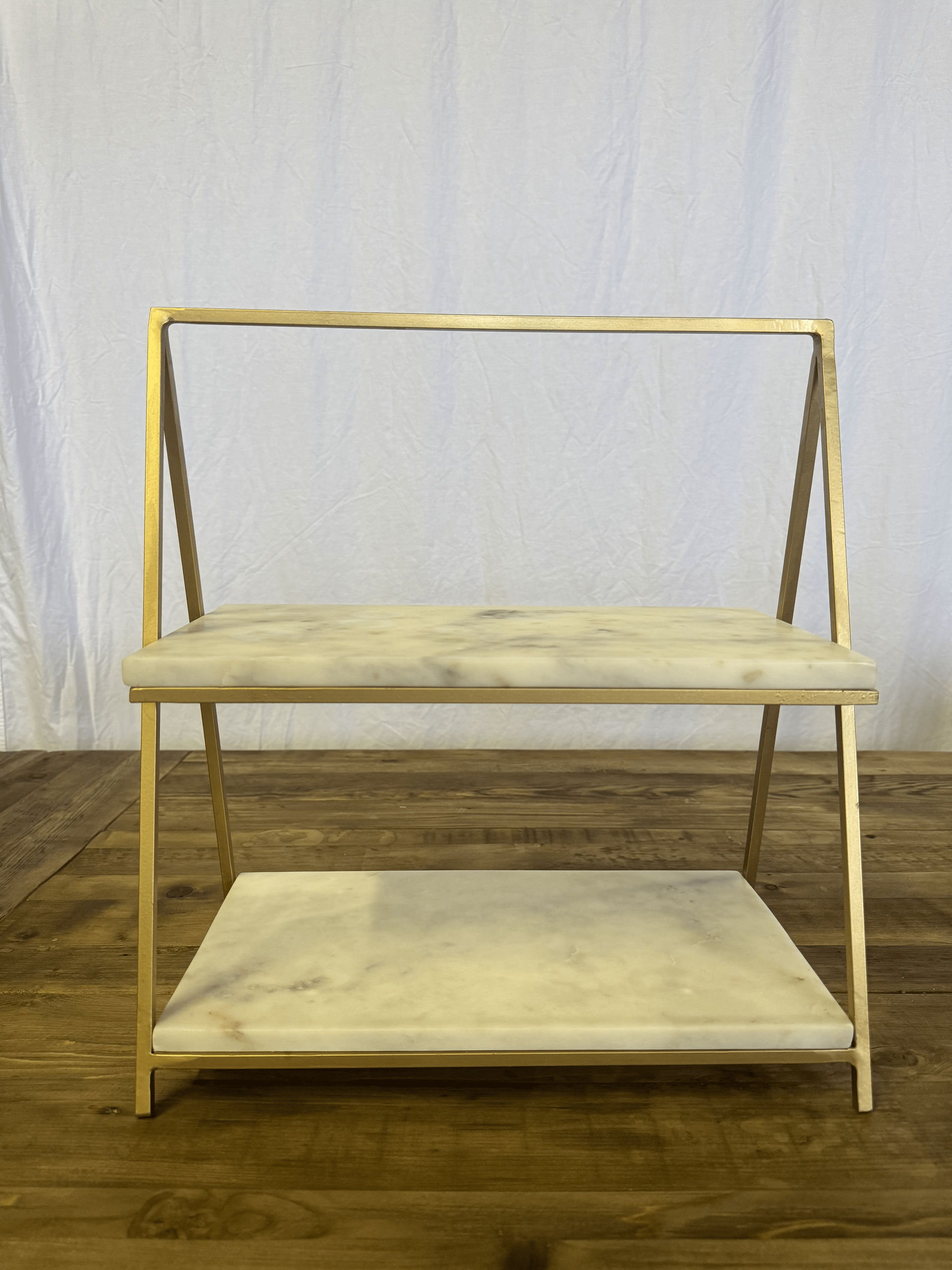 Light wood folding shelf with two beige shelves against a white curtain backdrop