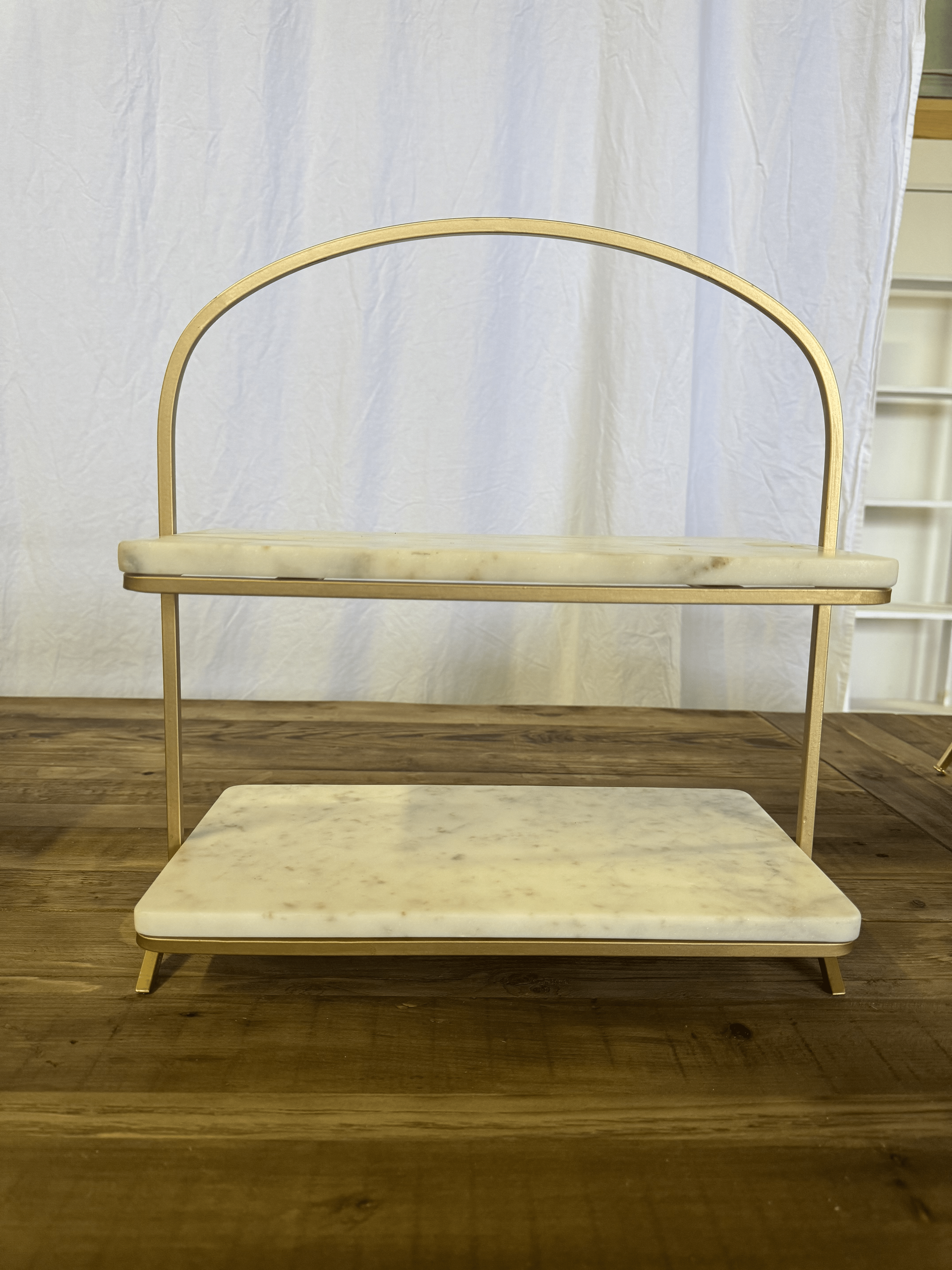 Wooden two-tier shelf or bench against a white curtain on a hardwood floor