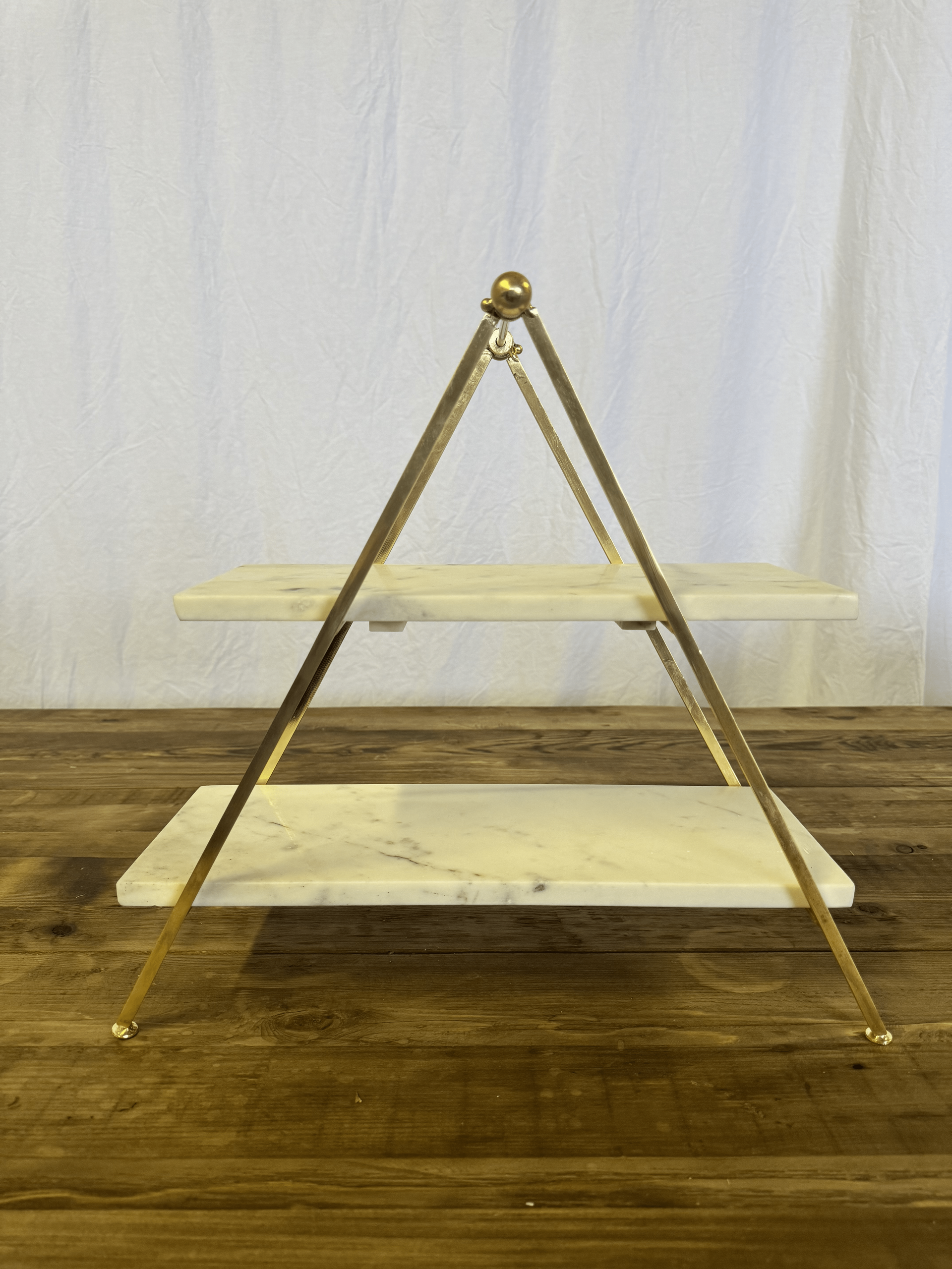A wooden triangular easel-style stand with two shelves against a white backdrop.