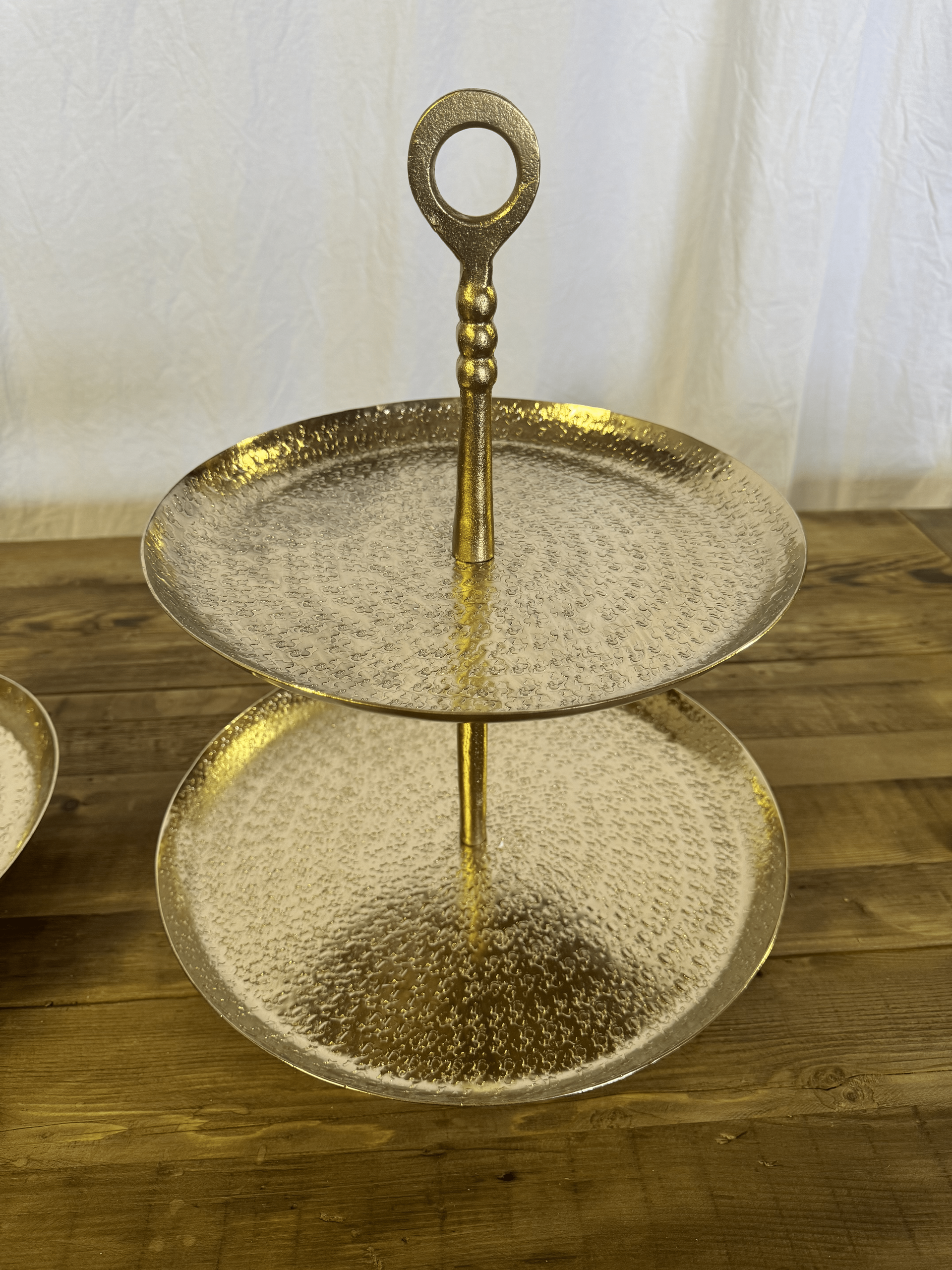 Two-tier gold metal serving stand with textured glass plates on a wooden table