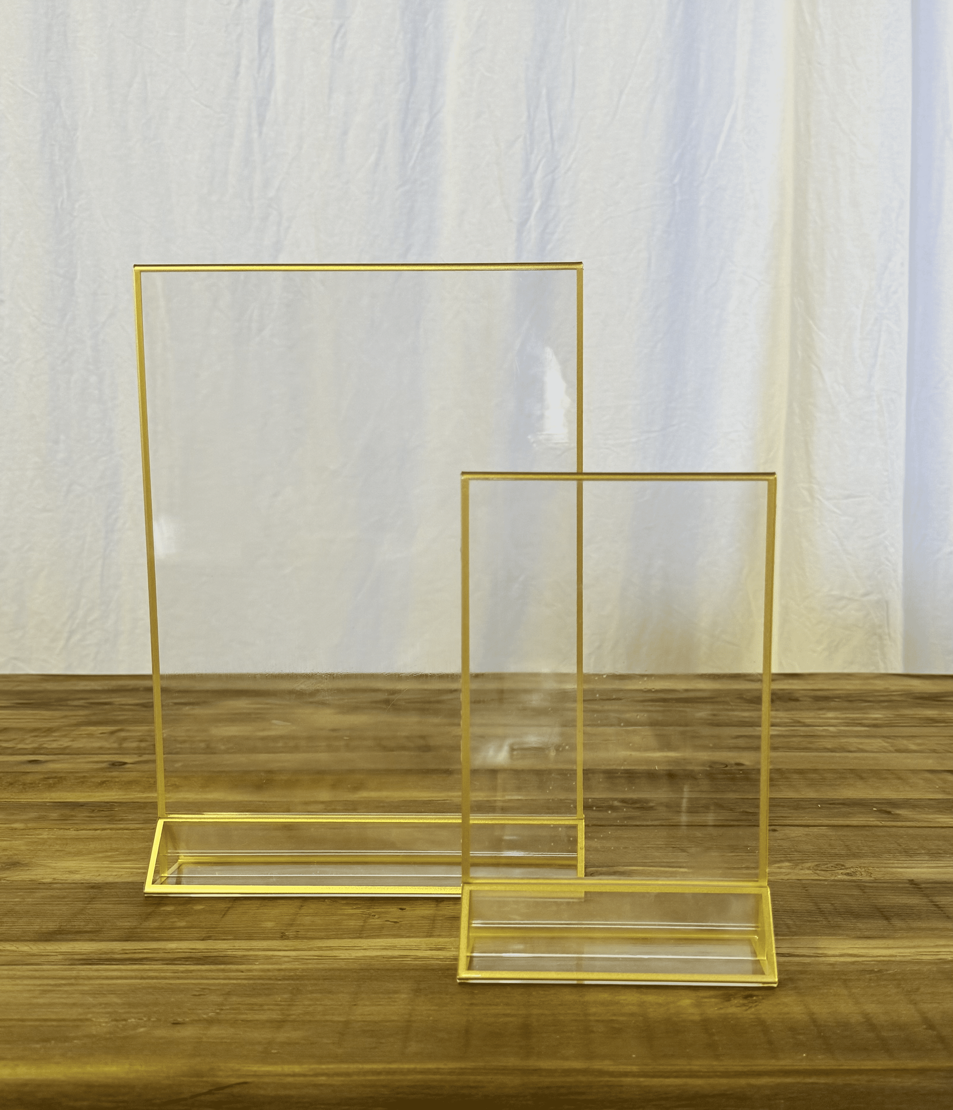 Two gold metal display frames on a wooden floor against a white curtain backdrop