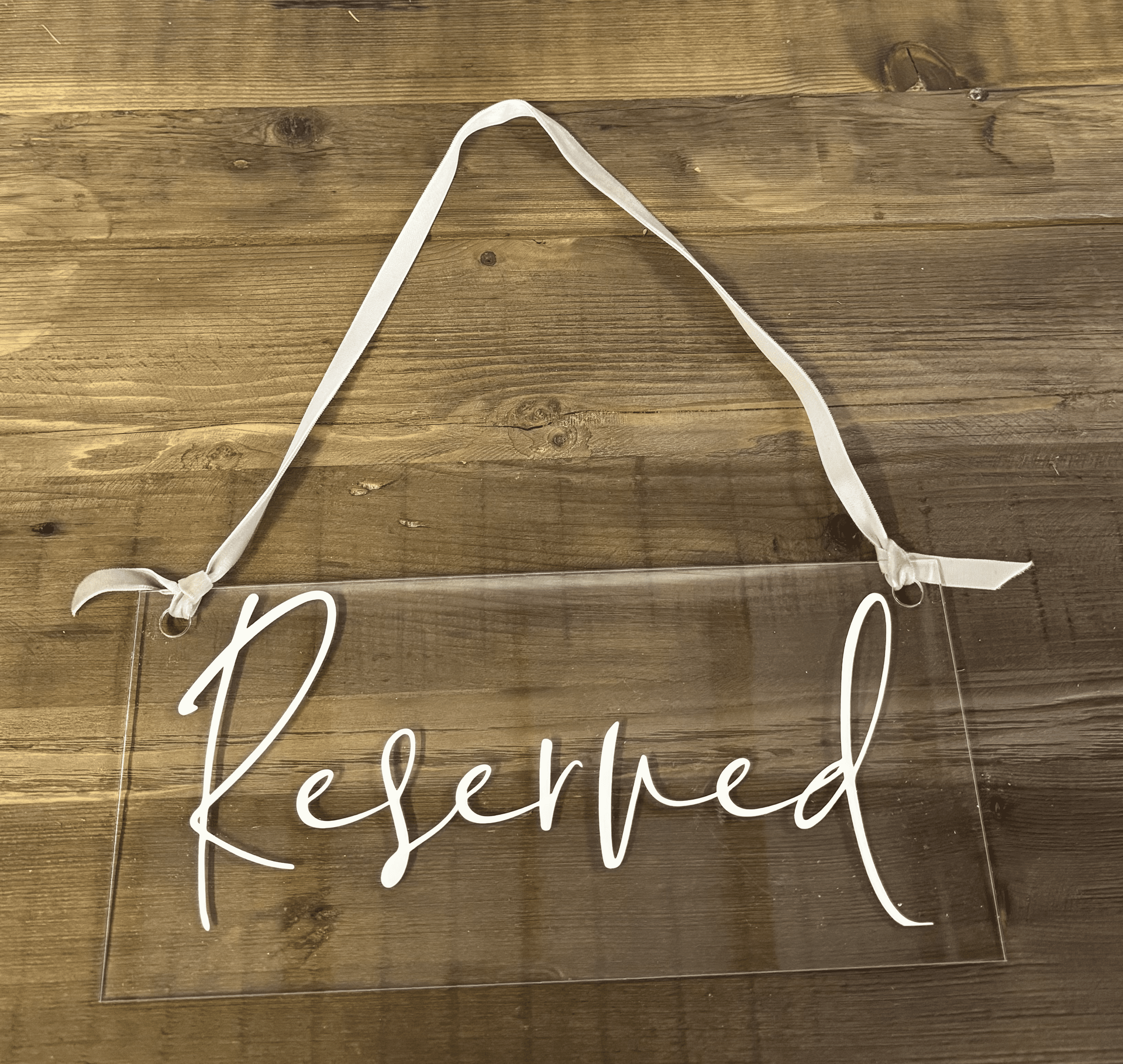 Reserved sign on a clear chair with white ribbon handles on a wooden surface