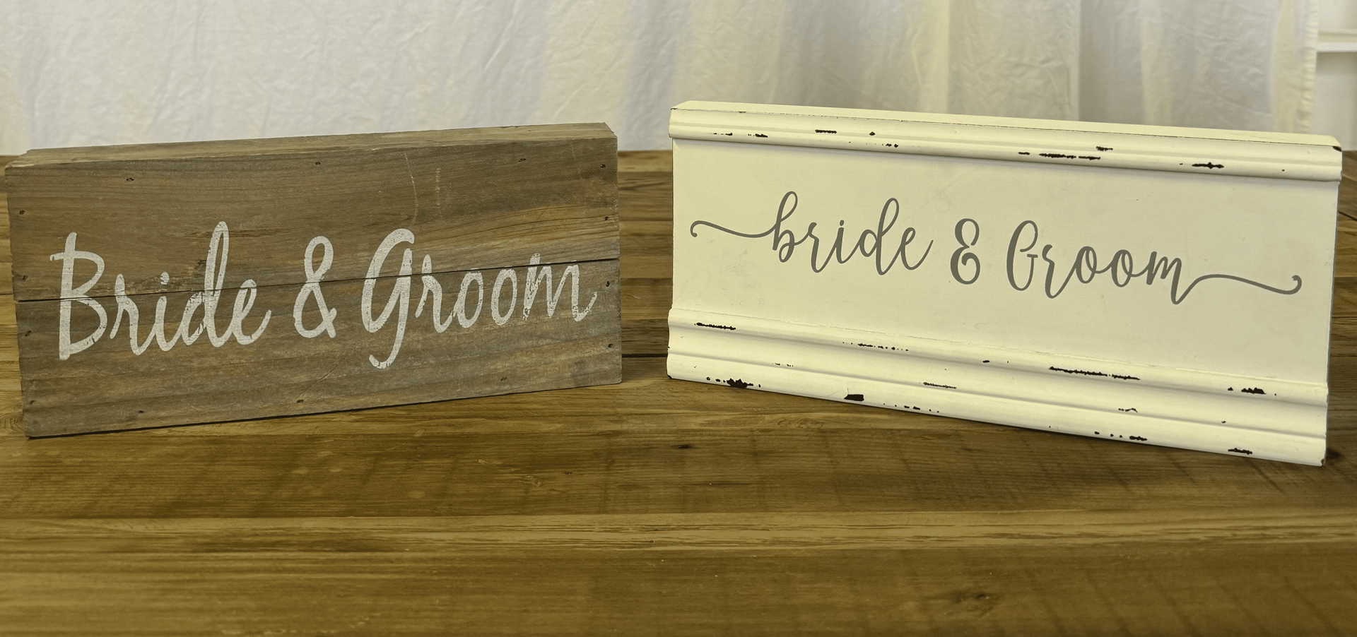 Two rustic wooden bride and groom signs, one gray and one white, on a table.