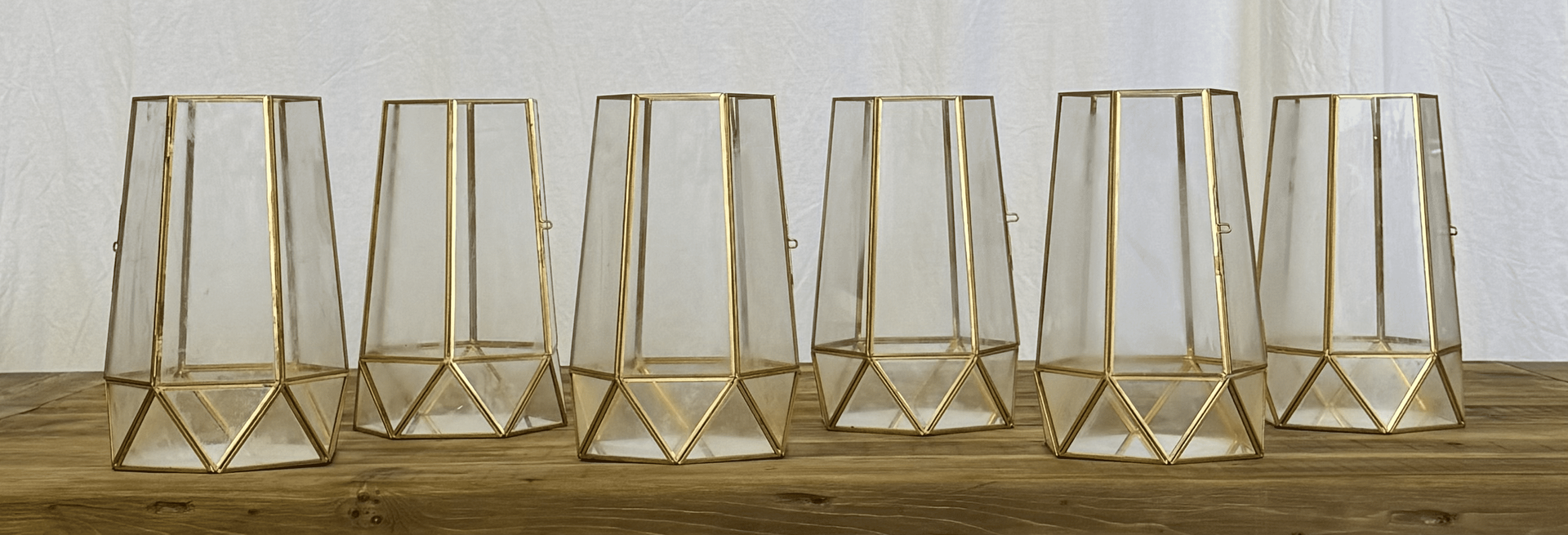 Six gold wireframe candle holders lined up on a white surface