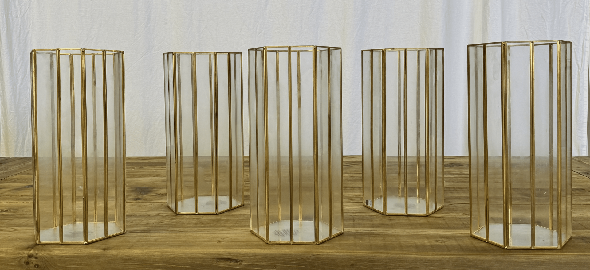 Three gold wireframe pedestal-like frames arranged on a wooden floor against a light wall.