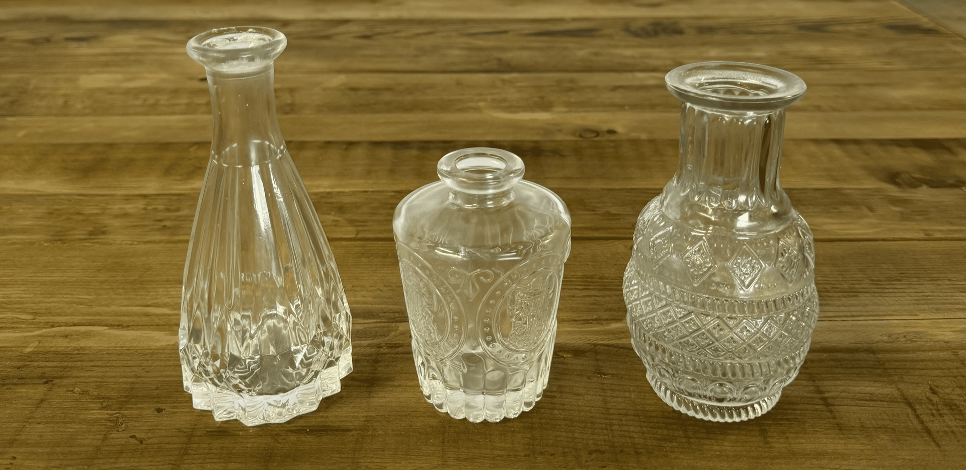 Three clear glass vases of different shapes on a wooden table