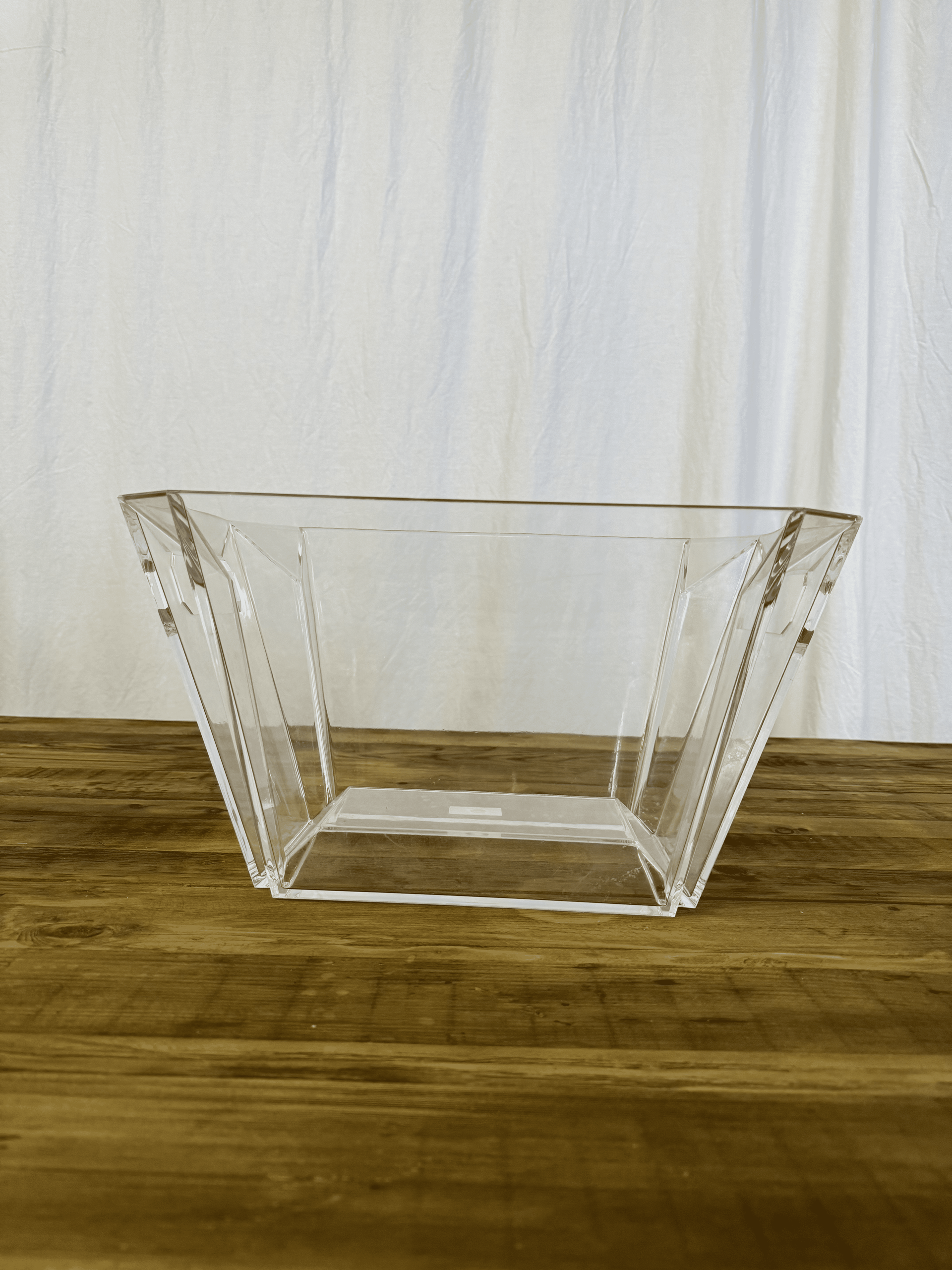Clear glass trapezoid bowl on a wooden surface in front of a white curtain