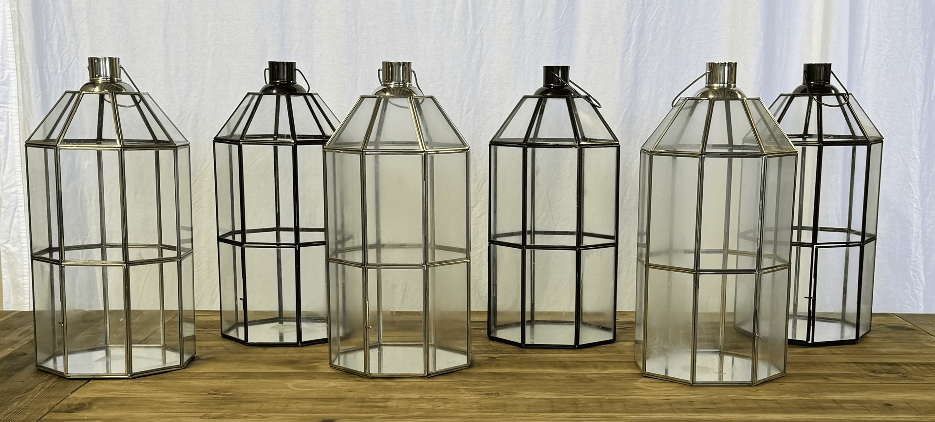 Five small white metal birdcage lanterns lined up on a wooden surface against a plain wall
