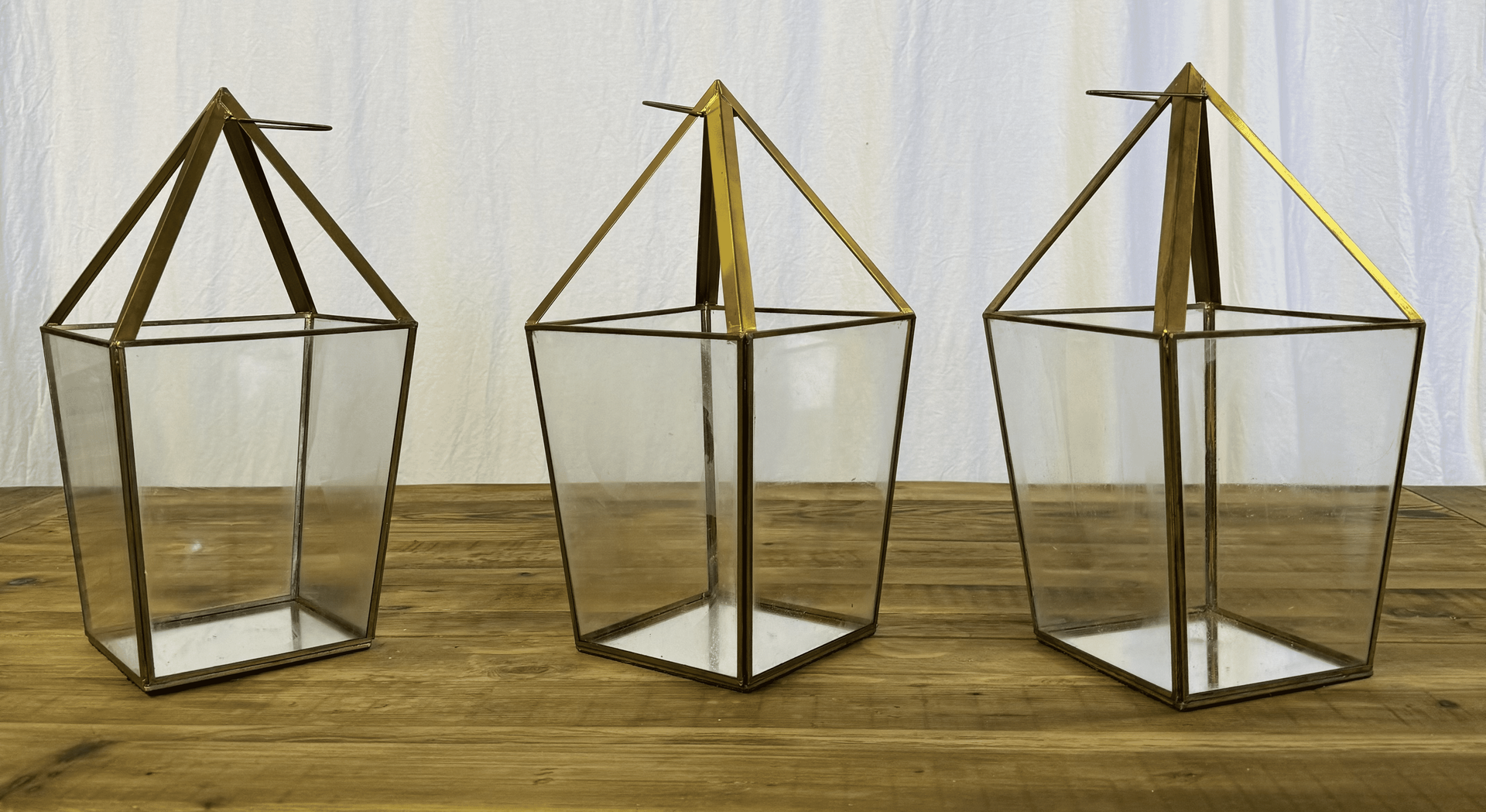 Three geometric wire lantern frames on a wooden surface, with dark and yellow tops.