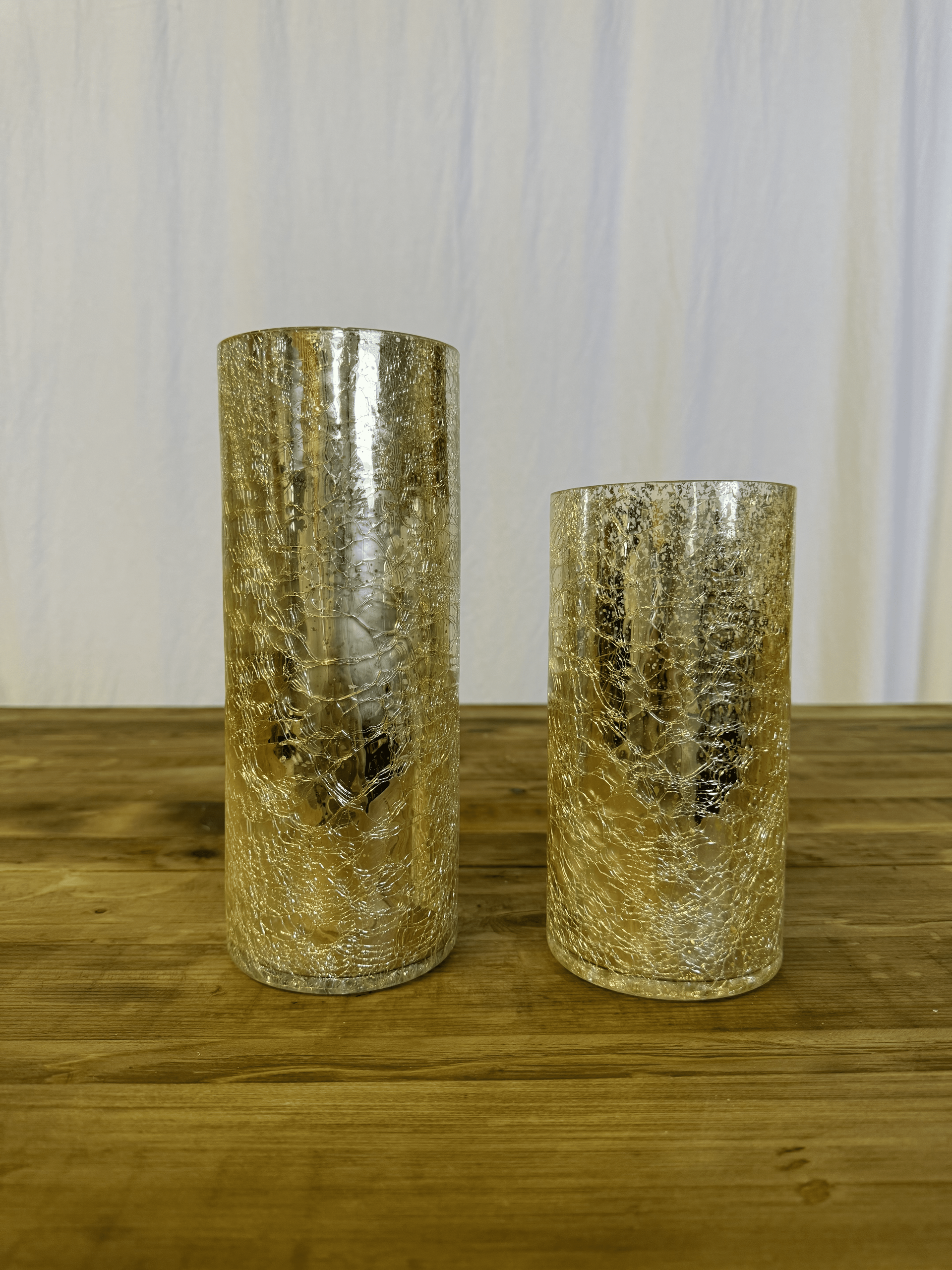 Two gold glitter candle holders on a wooden surface against a light curtain backdrop