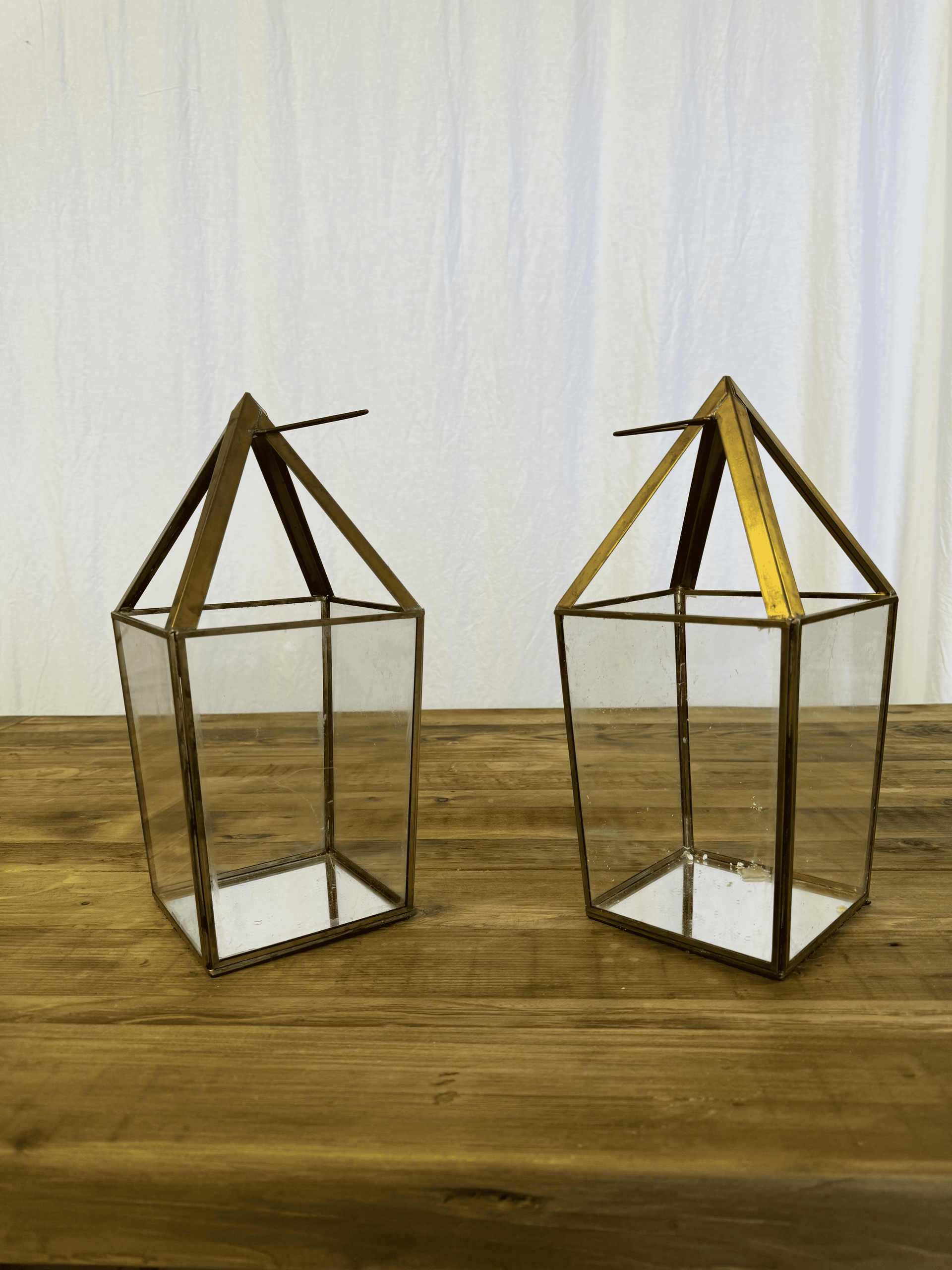 Two small metal lantern frames on a wooden table against a plain light background.