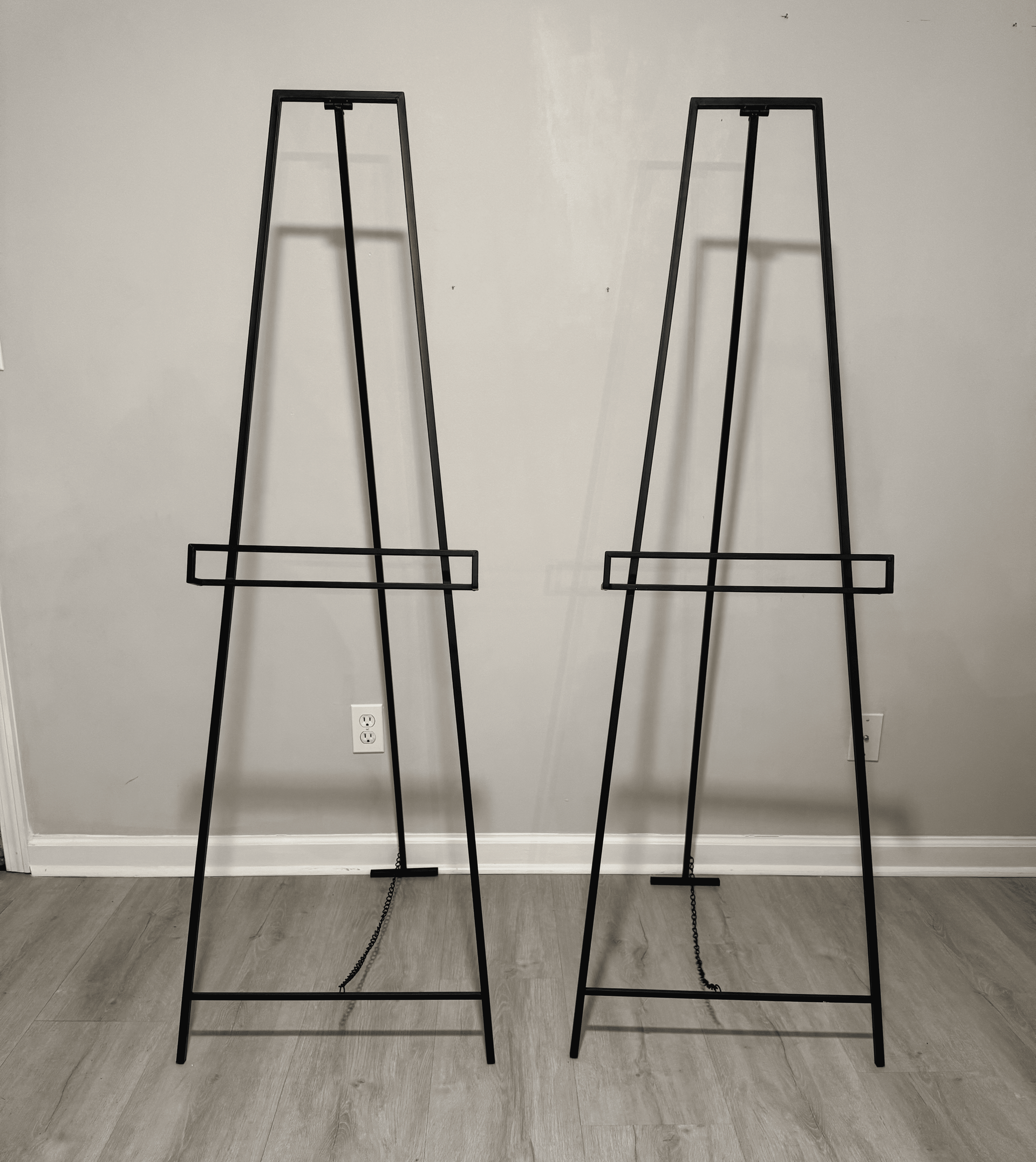 Two black wire frame stands leaning against a white wall on a carpeted floor.