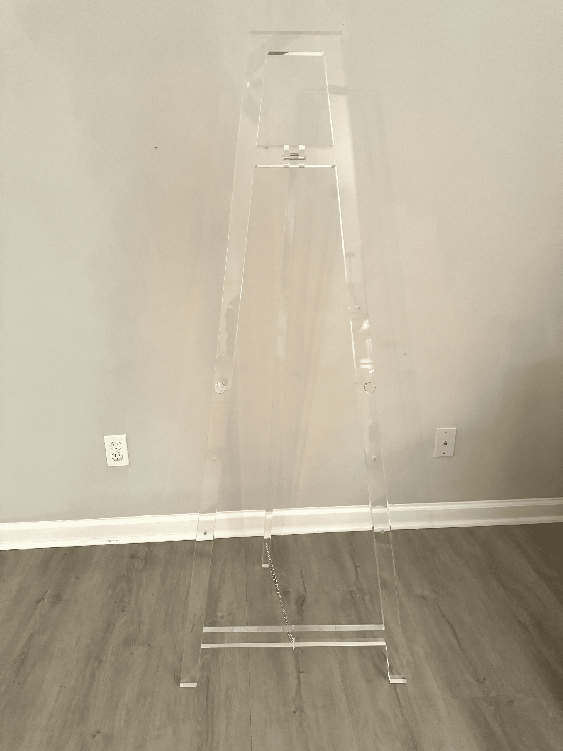 Clear acrylic clothing rack stand against a gray wall in an empty room.