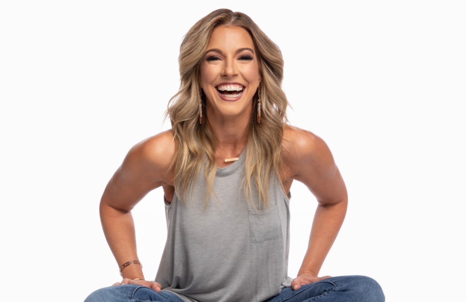 Smiling woman in a gray tank top sitting cross-legged against a white background