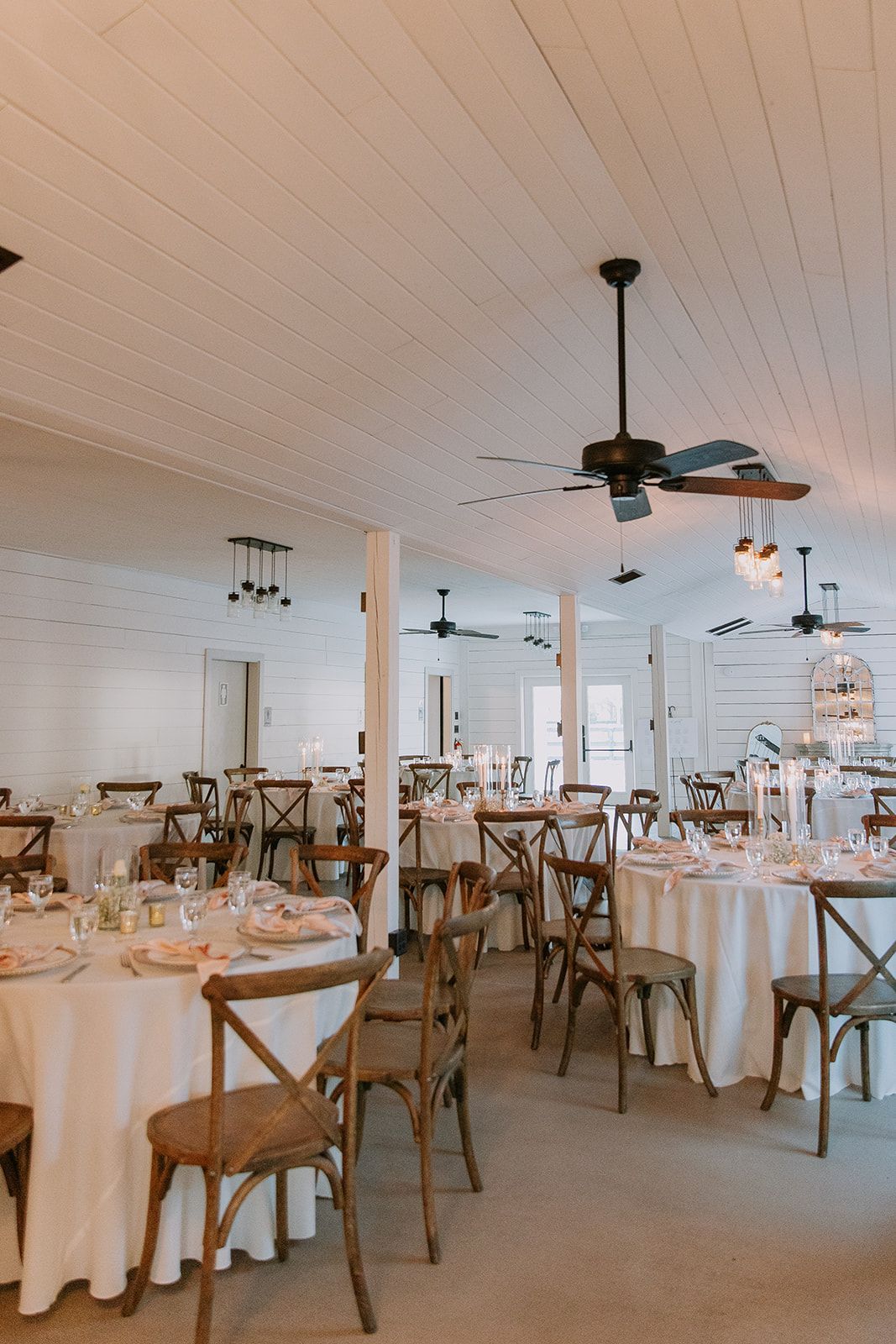 Bright dining room with set tables, wooden chairs, white tablecloths, and ceiling fans.