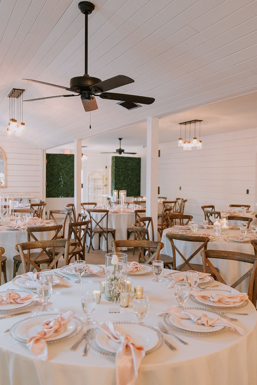 Elegant dining room with round white table settings, wooden chairs, and ceiling fans in a bright space