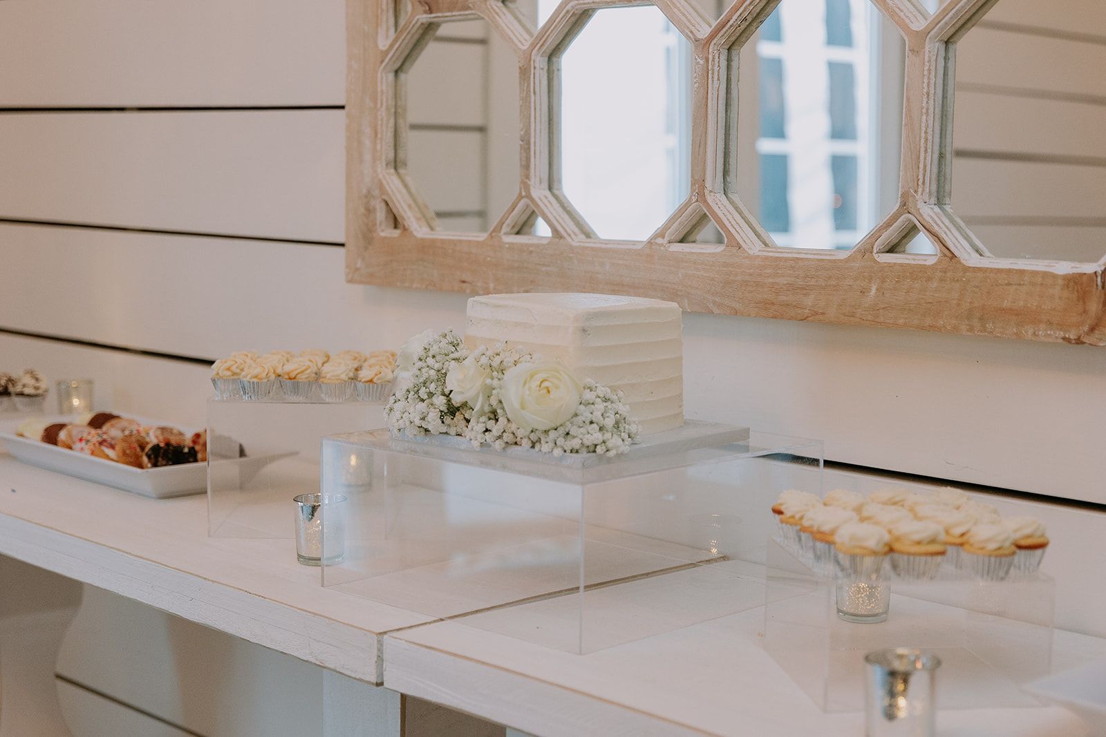 Elegant dessert table with white flowers, cakes, and pastries in a bright room with a mirrored wall panel