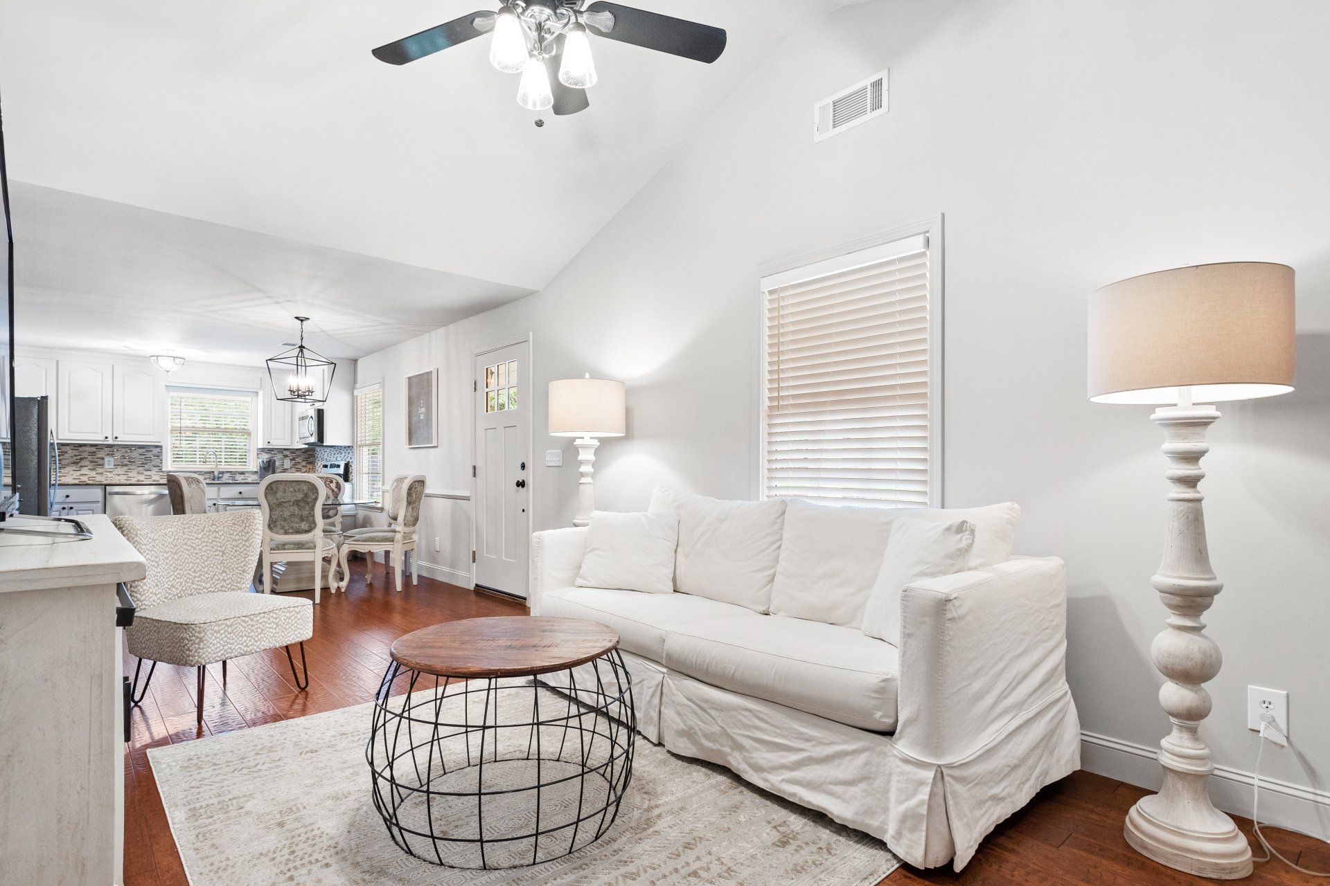 Bright living room with white sofa, round coffee table, floor lamp, and open dining area beyond.