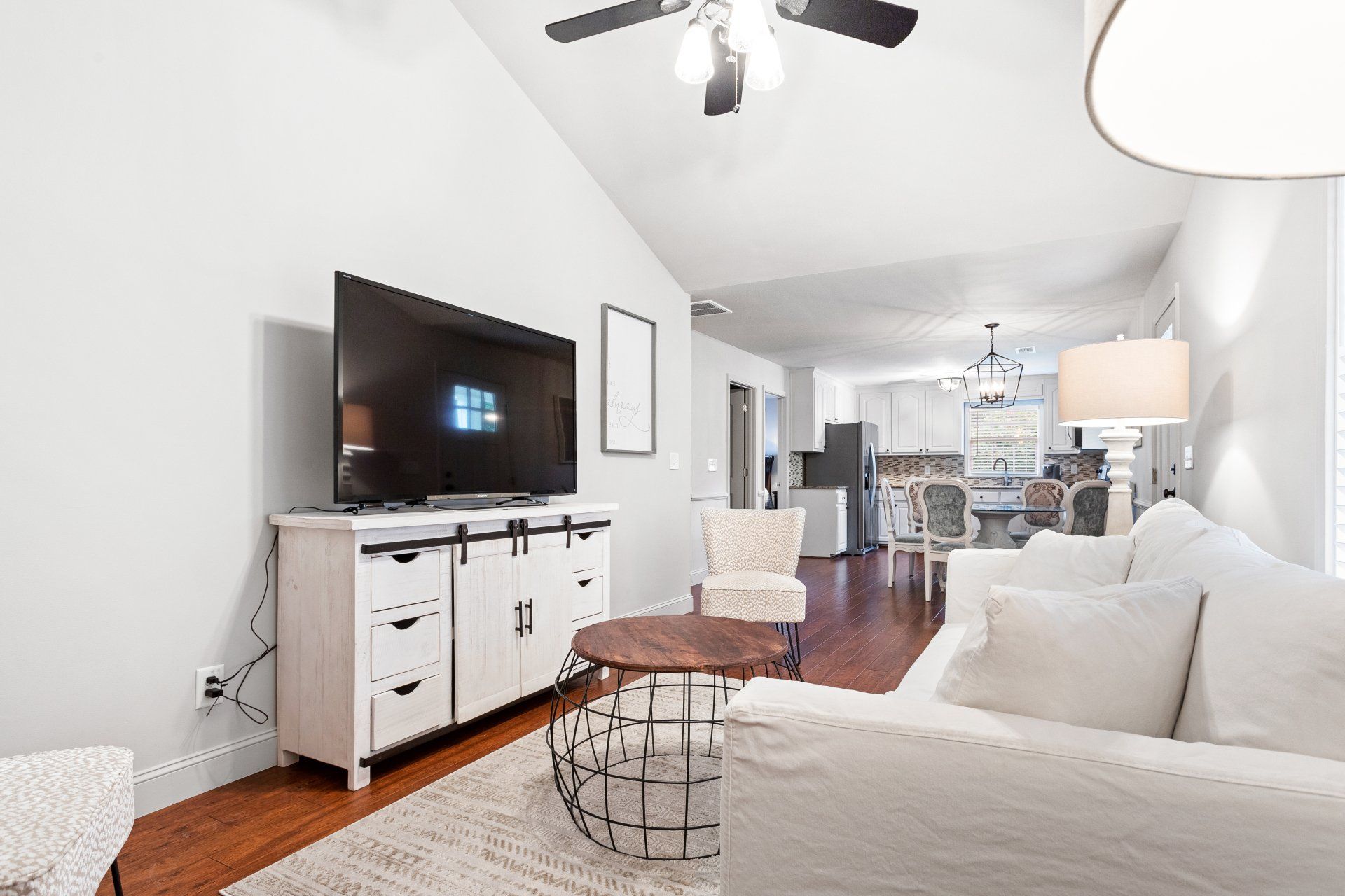 Bright living room with white sofa, TV on cabinet, round coffee table, and hardwood floors.