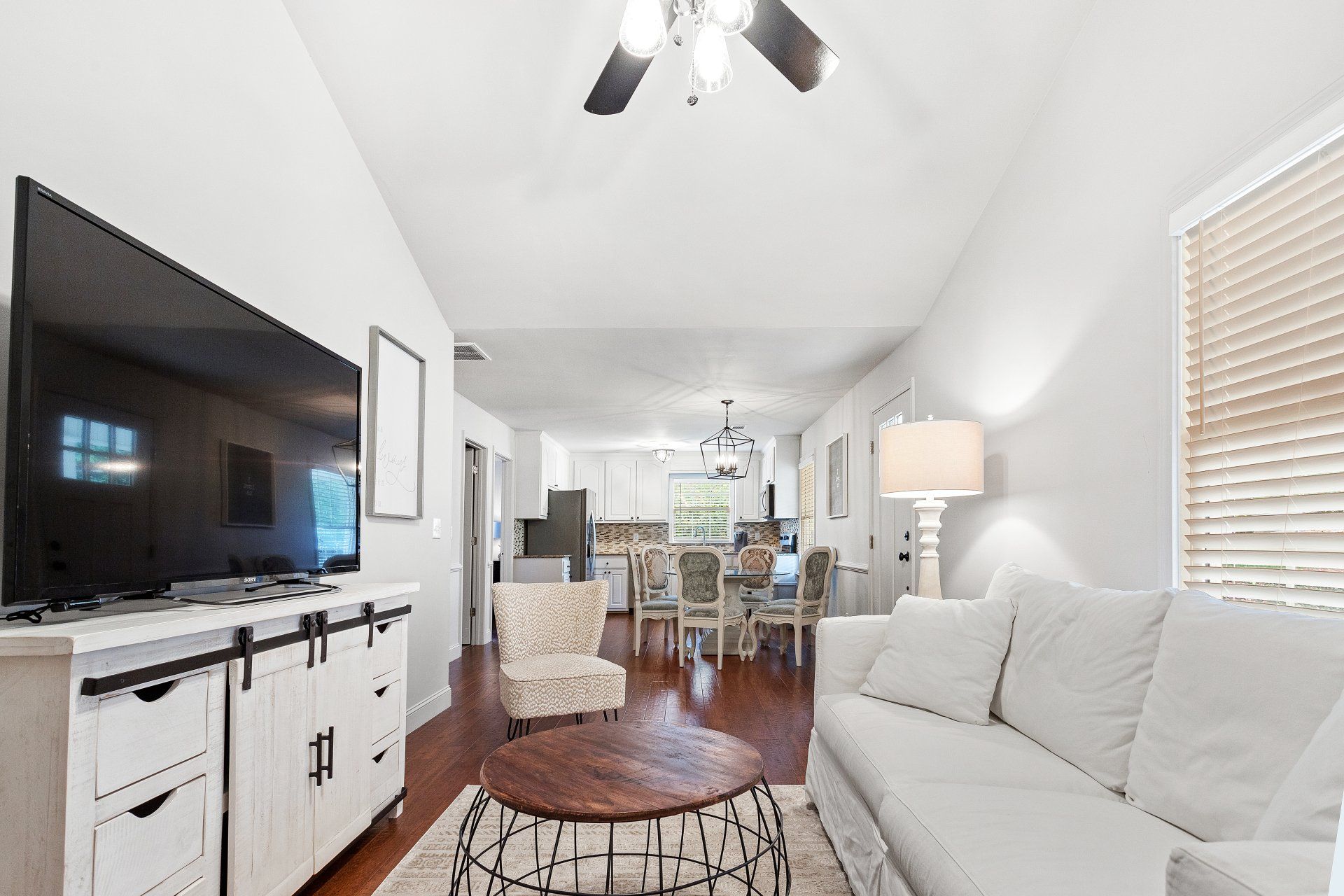 Bright living room with white sofa, TV, lamp, and dining area under a vaulted ceiling