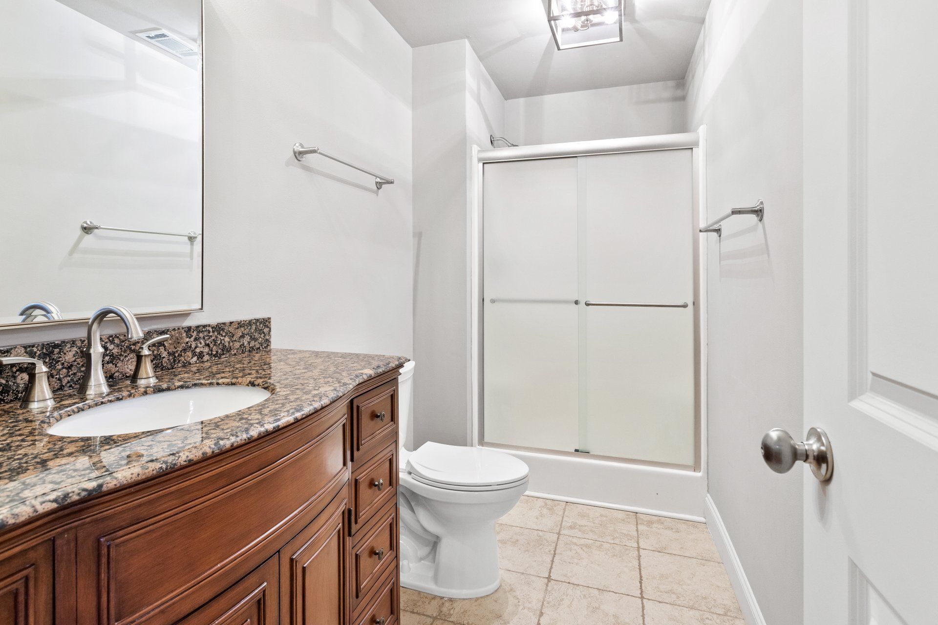 Bright bathroom with granite vanity, toilet, and frosted glass shower door
