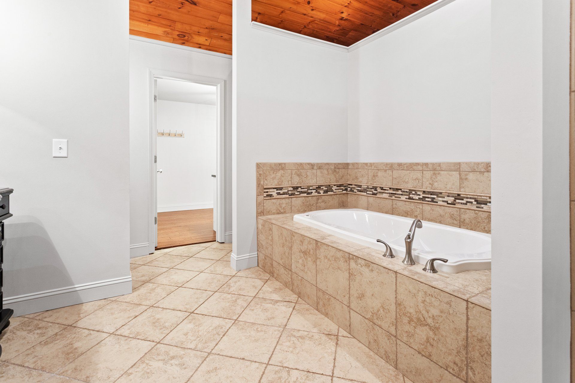 Tiled bathroom with a built-in tub, beige floors, white walls, and wood-paneled ceiling and doorway