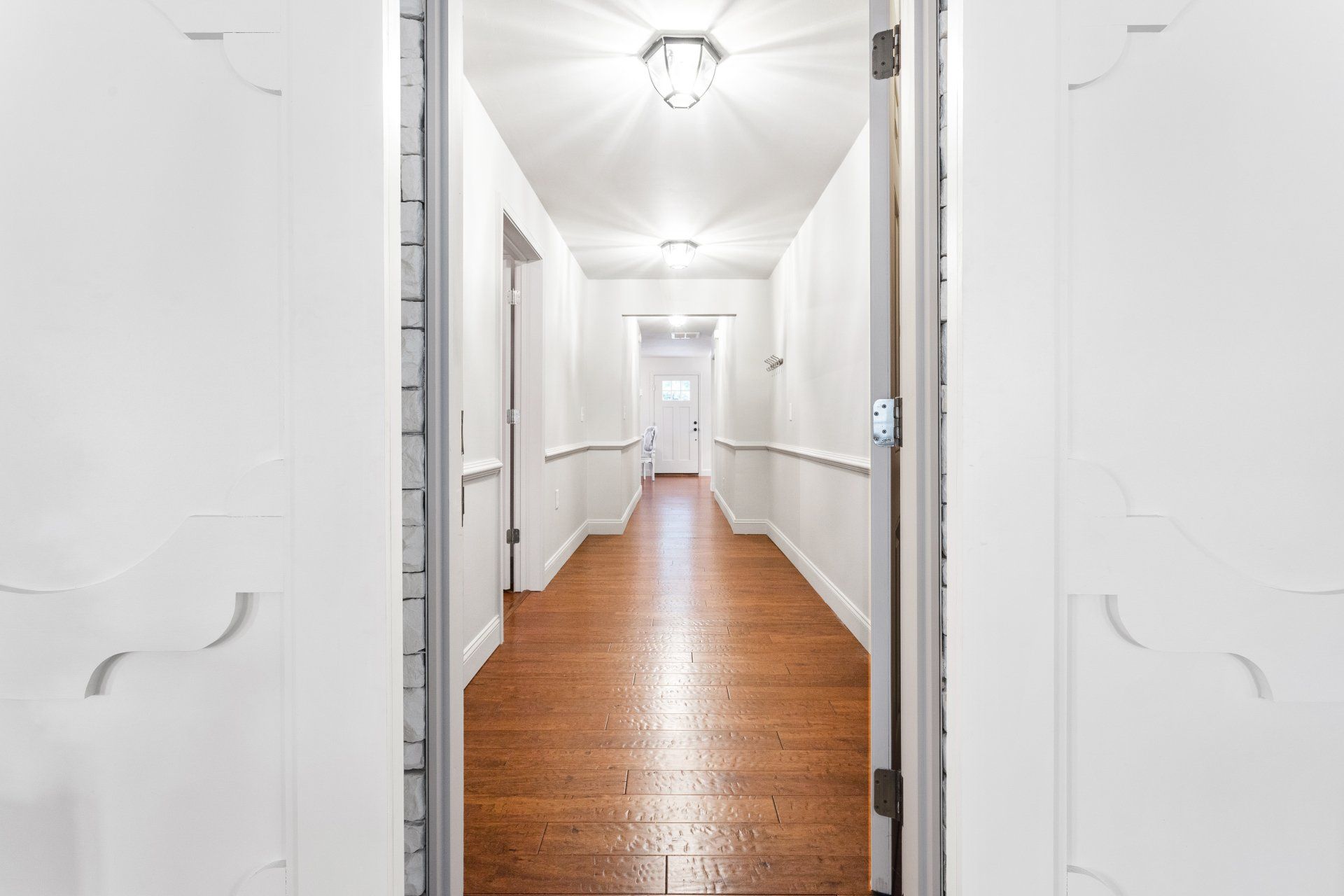 Bright white hallway with hardwood floor and doors on both sides, seen through an open doorway.