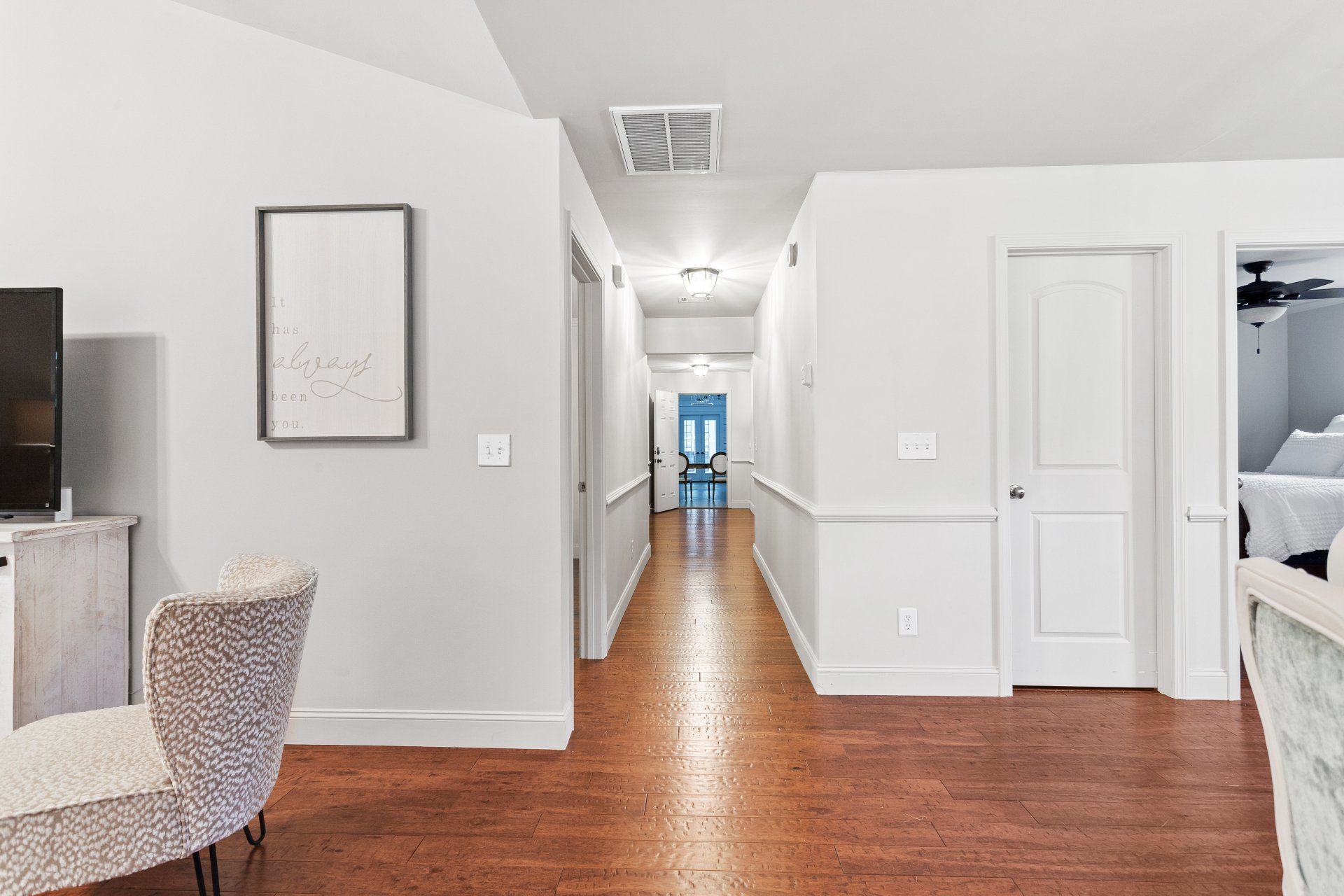 Bright hallway with hardwood floors, white walls, and a view into a blue room at the far end