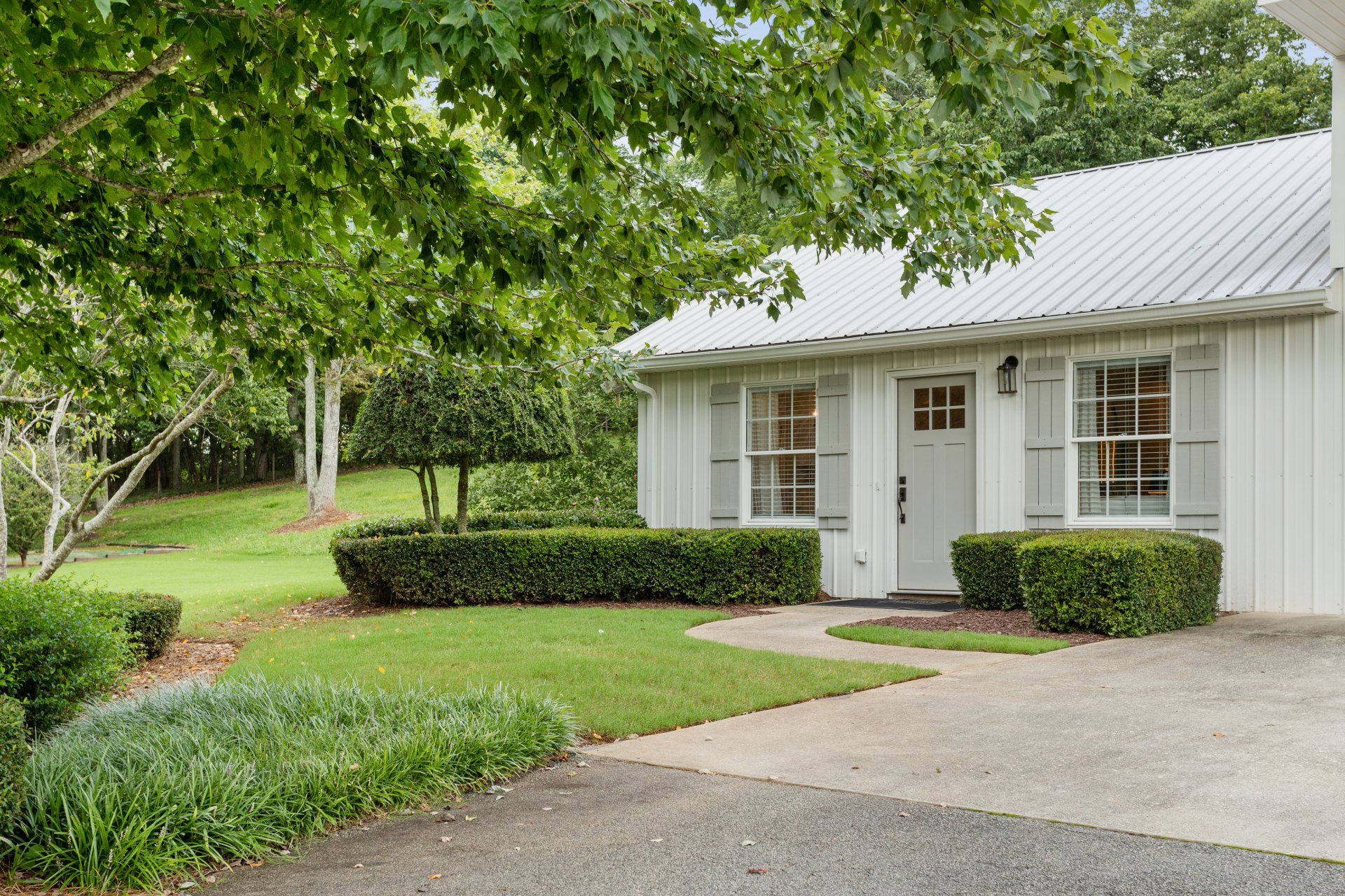 White house with front porch, green lawn, and trees beside a driveway