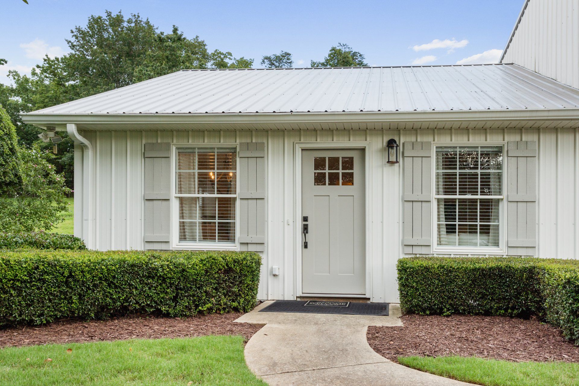 Small white cottage with a front door, two windows, hedges, and a curved walkway.