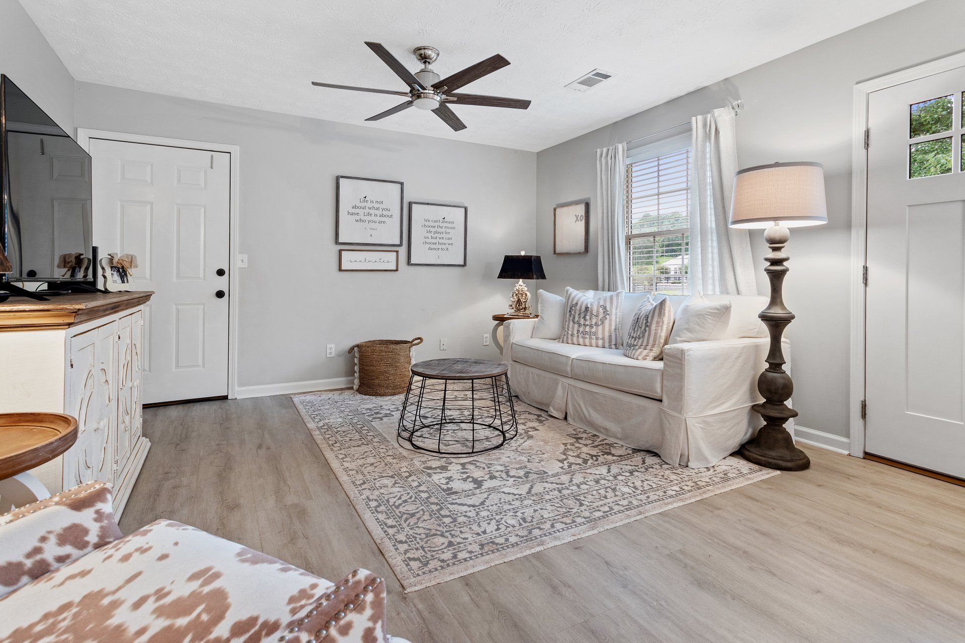 Bright living room with sofa, rug, floor lamp, ceiling fan, and French doors to a patio.