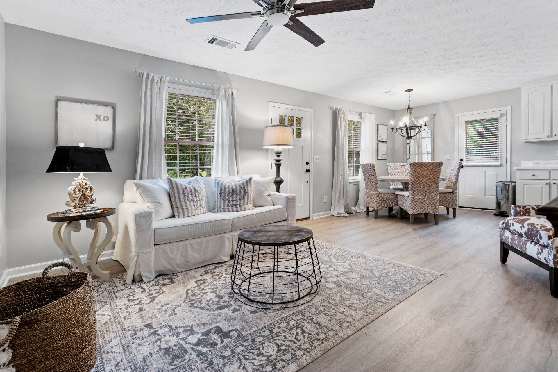 Bright open living room with white sofa, patterned rug, round coffee table, and dining area beyond.