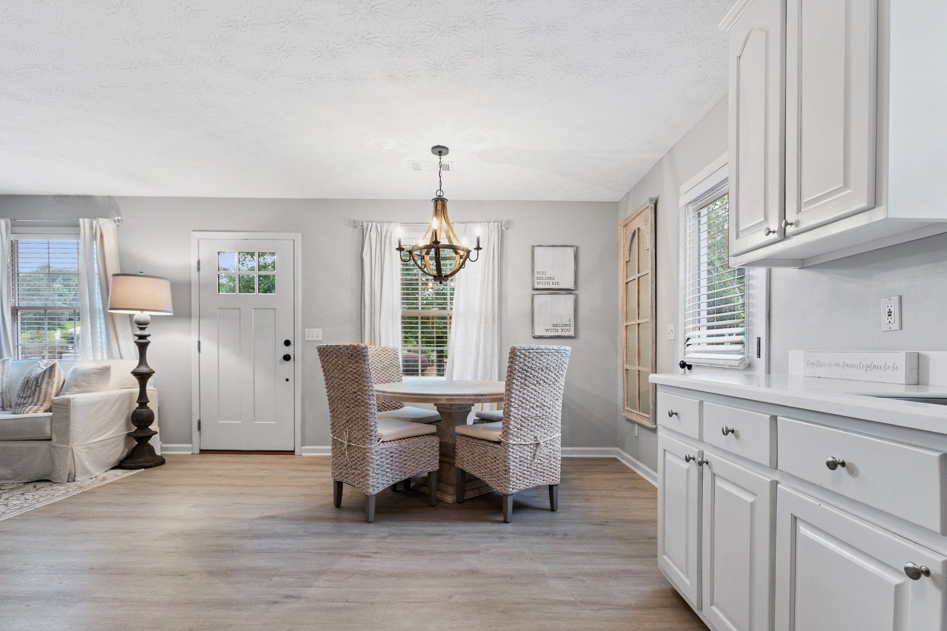 Bright dining area with white cabinets, round table, and chairs in a sunlit kitchen-living space