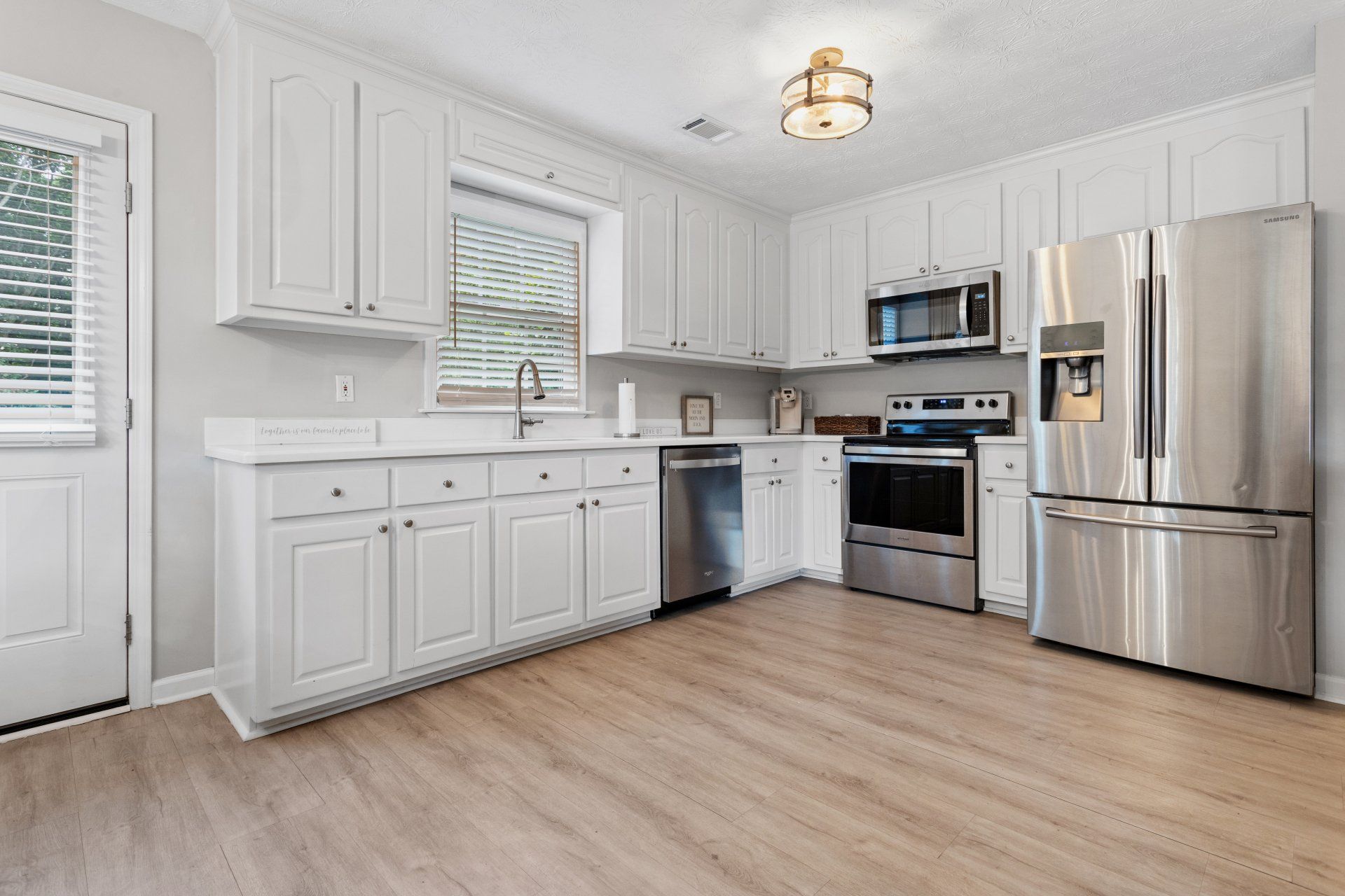Bright white kitchen with stainless steel appliances, light wood floors, and a window over the sink