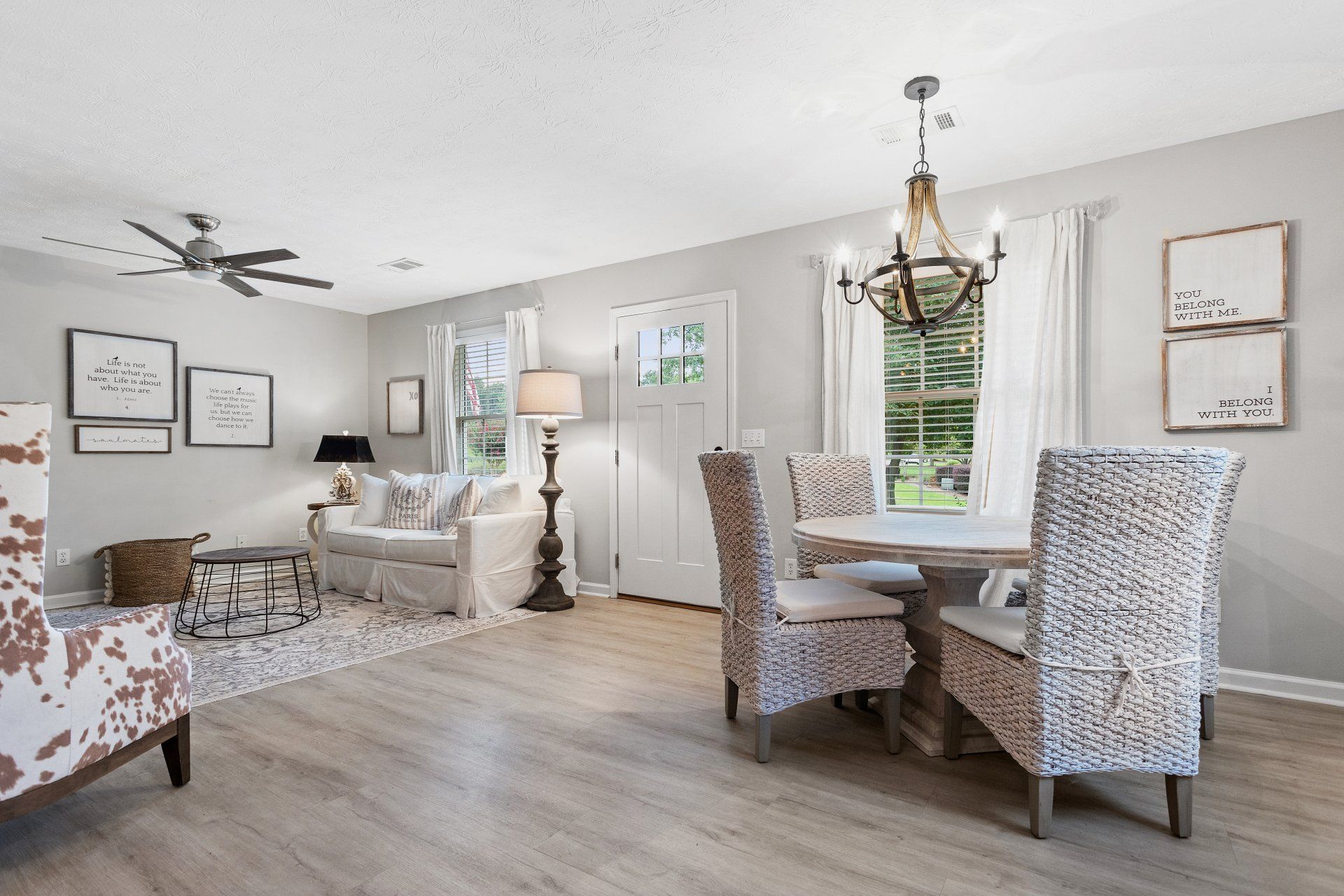 Bright living and dining room with floral chairs, white walls, hardwood floors, and a ceiling fan