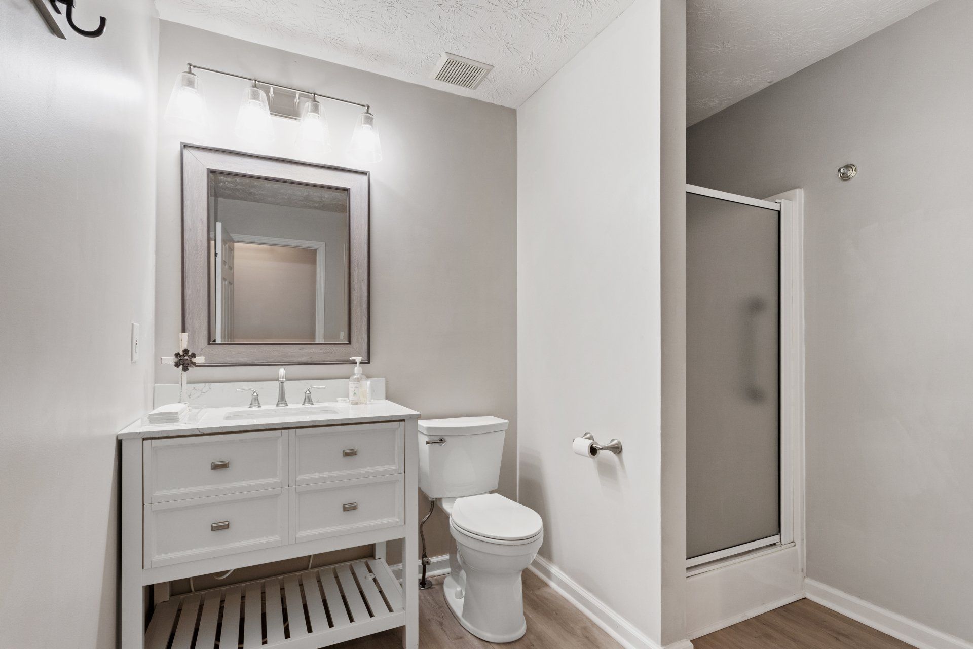 Modern bathroom with white vanity, mirror, toilet, and glass-enclosed shower in gray tones