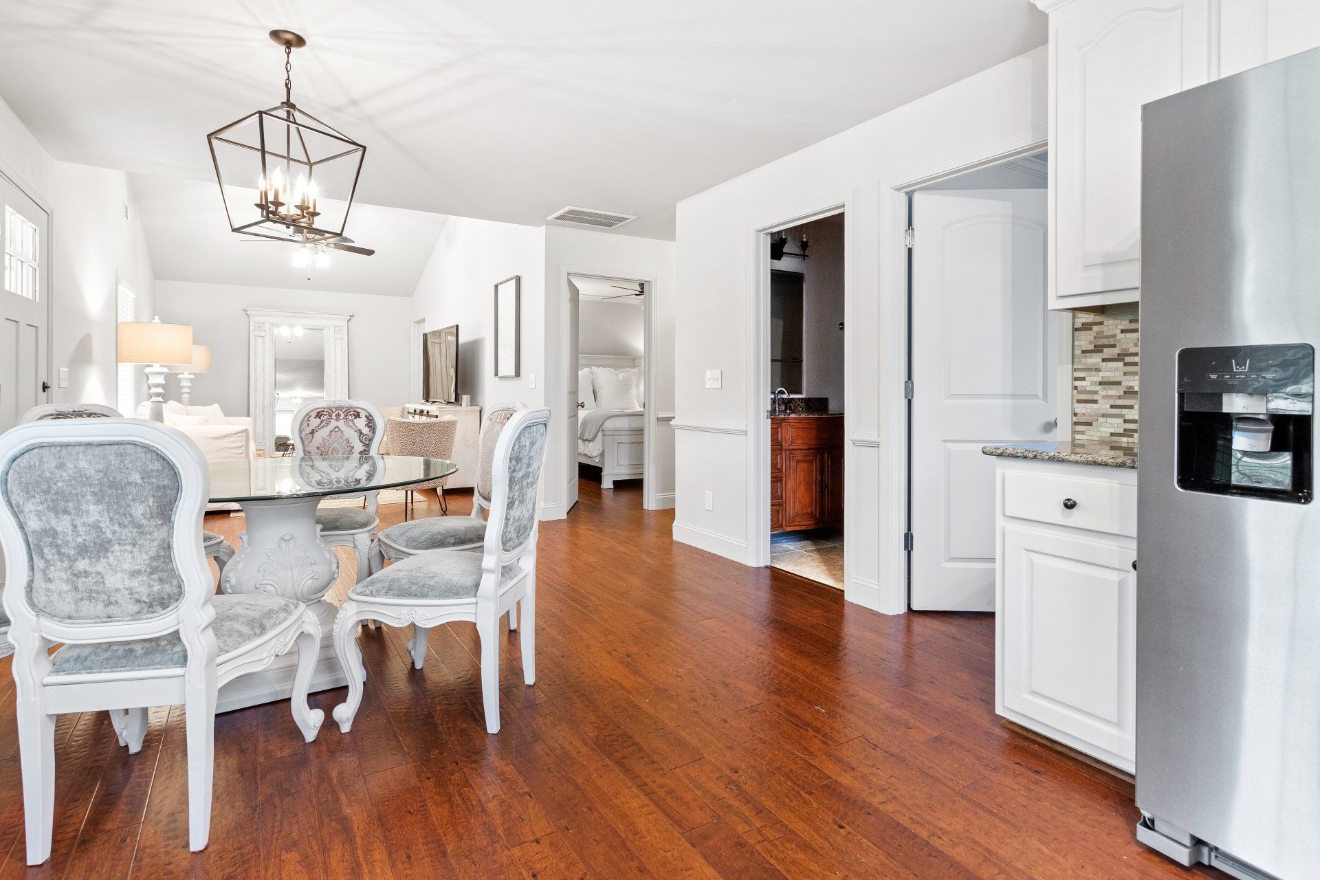 Bright dining room with white chairs, hardwood floors, chandelier, and stainless steel refrigerator.