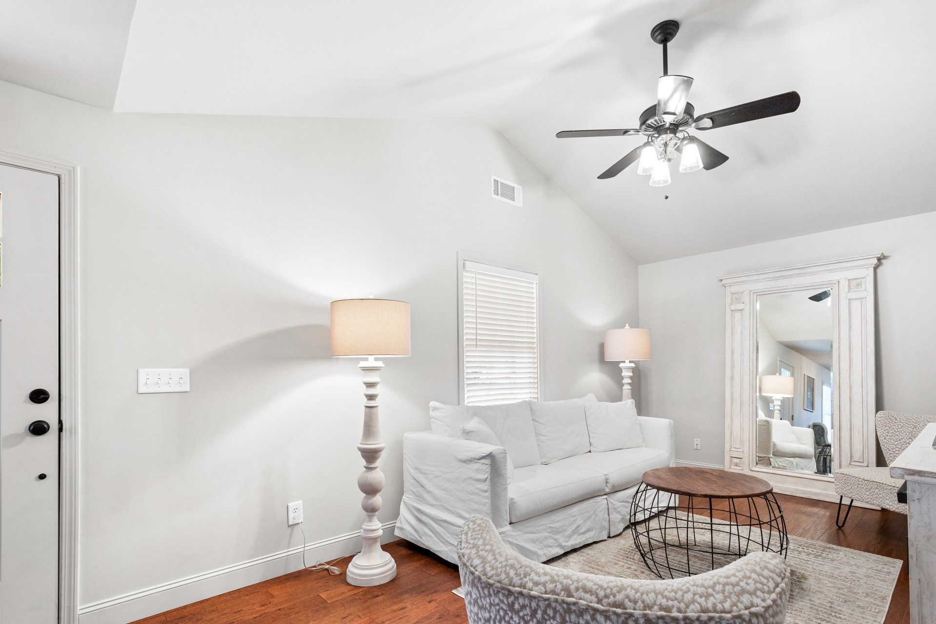 Bright white living room with sofa, floor lamp, mirrored cabinet, coffee table, and ceiling fan