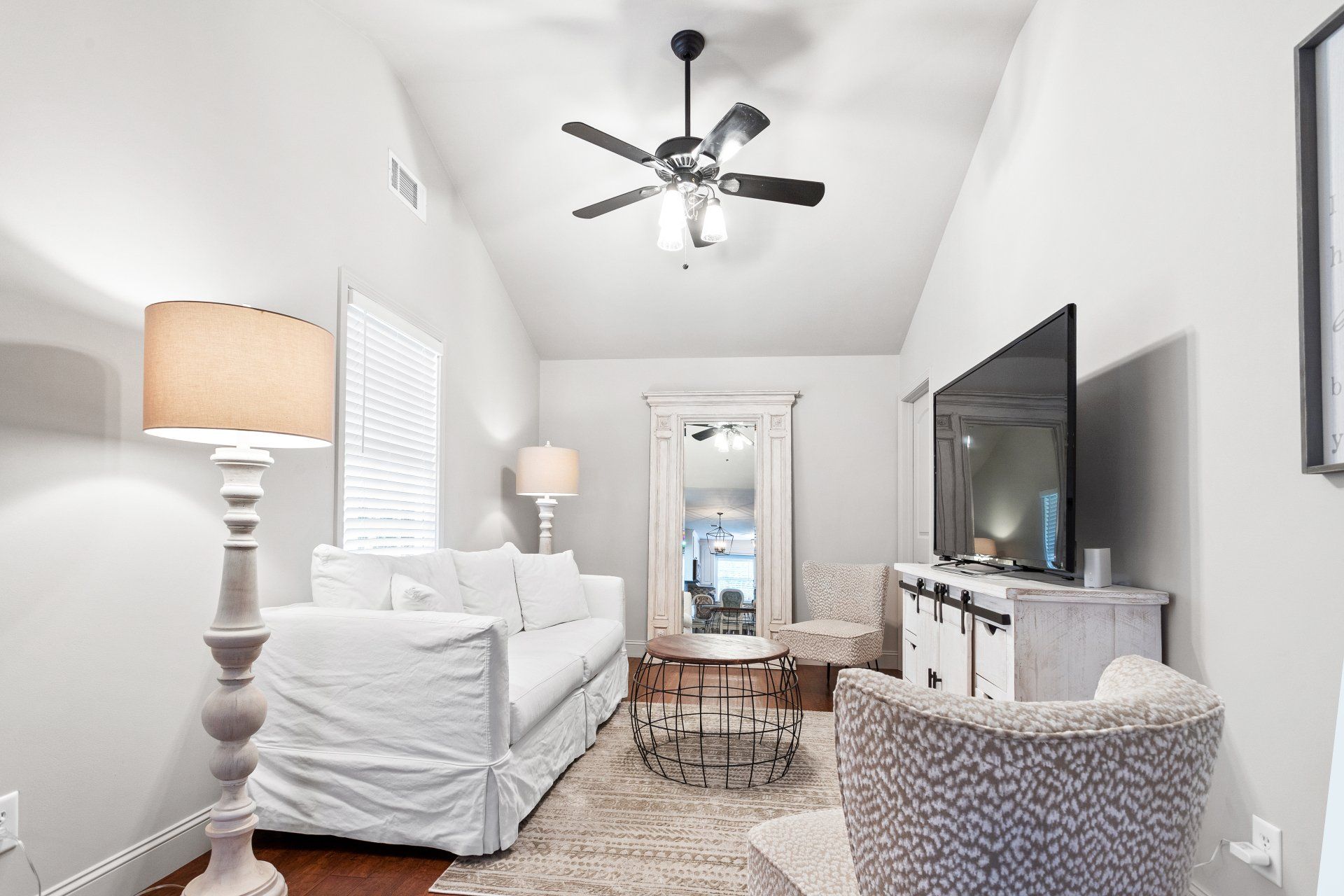 Bright living room with white sofa, TV, lamps, rug, and ceiling fan