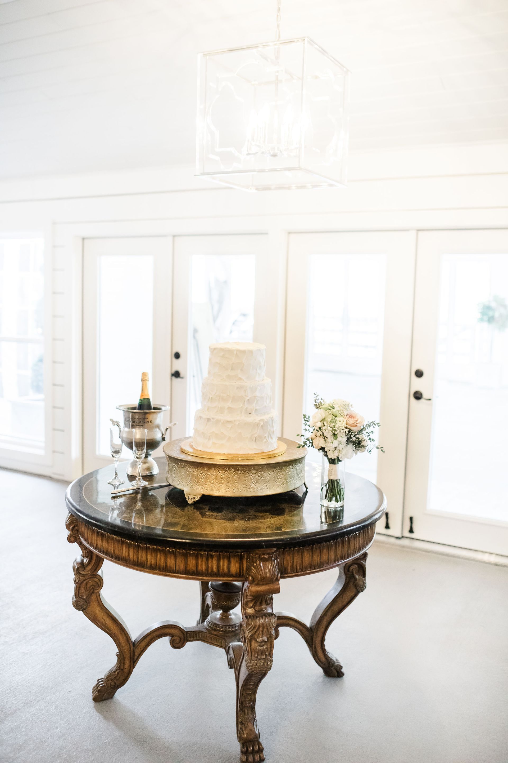 Ornate round table with a tiered cake in a bright white room with large windows