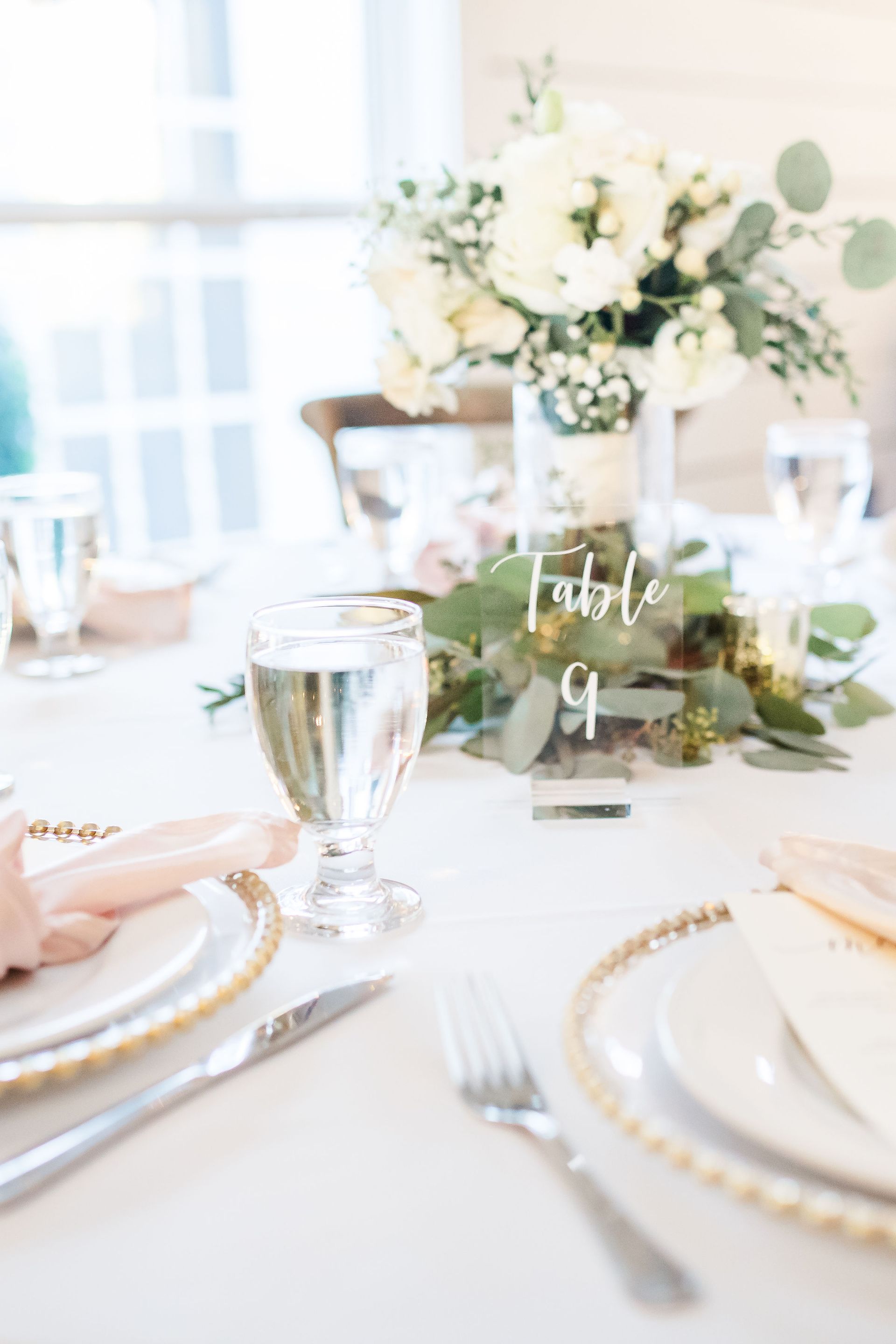 Elegant white-and-gold table setting with flowers and glassware at a bright event