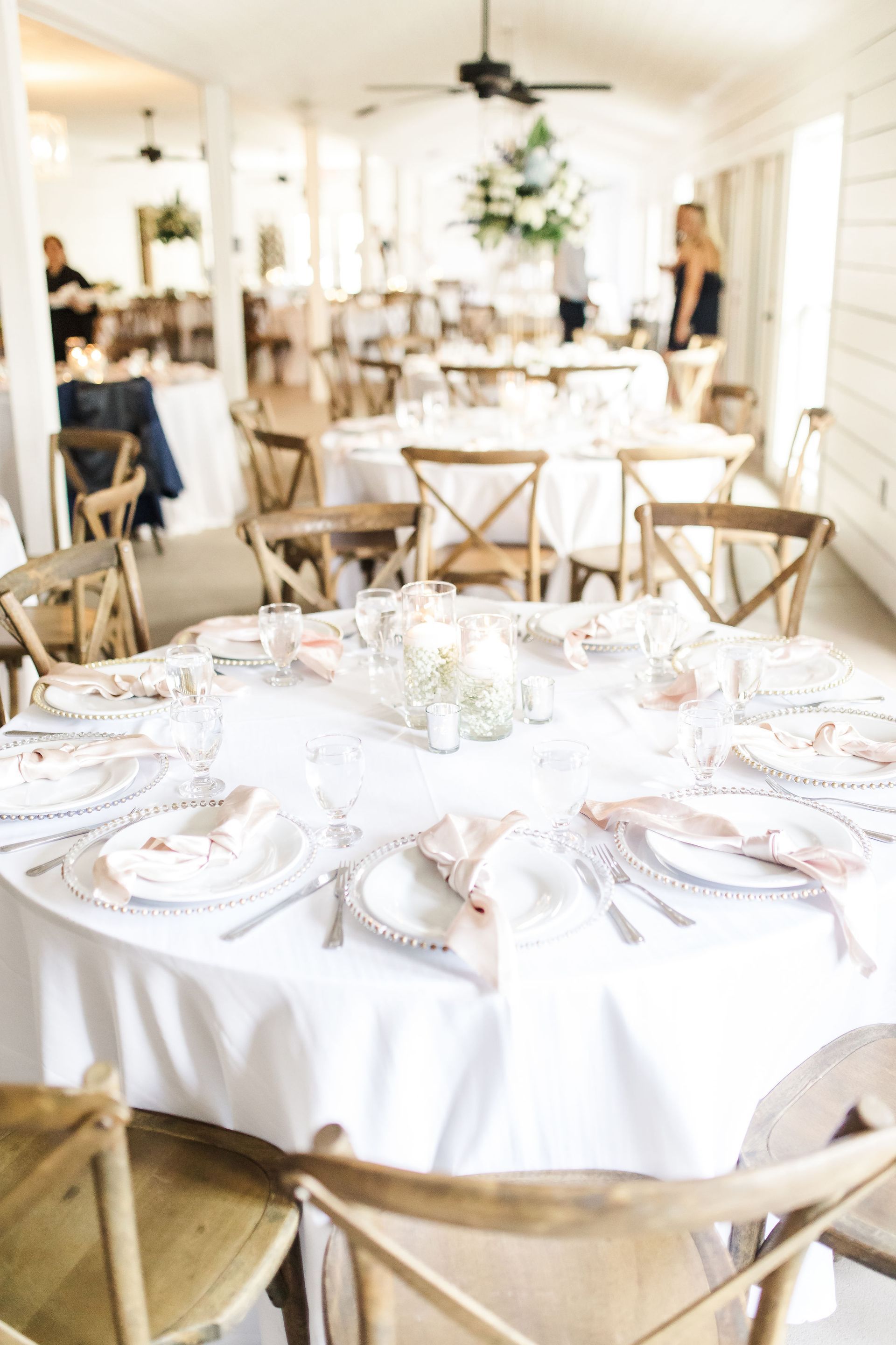 Elegant white banquet table set for an event in a bright room with wooden chairs and floral decor