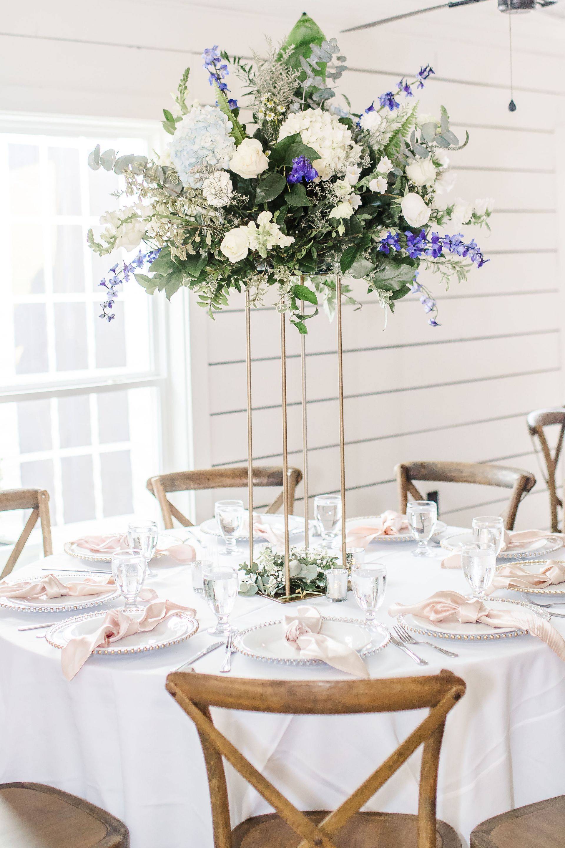 Tall white floral centerpiece with blue accents on a round table set for an elegant indoor event