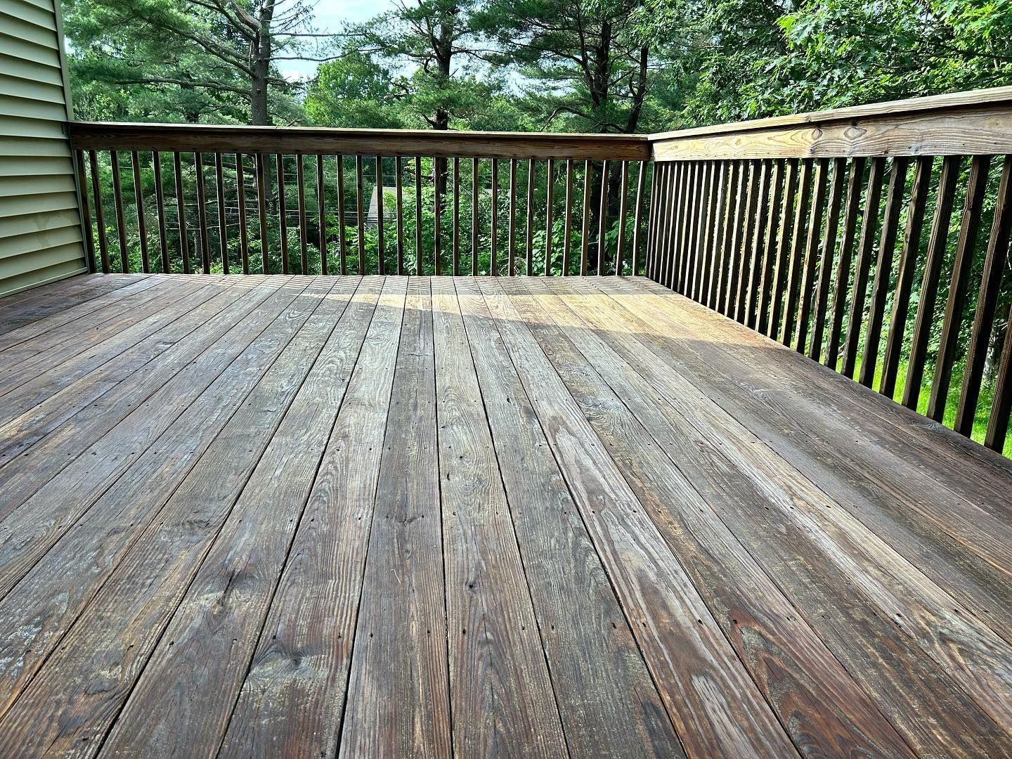 Wooden deck with railing, weathered and overlooking a green, tree-filled landscape.
