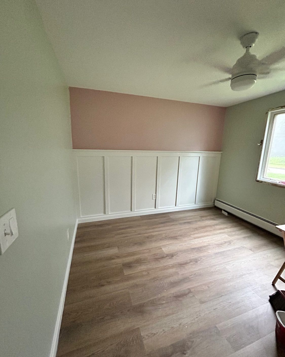Empty room with pink and white accent wall, wainscoting, and wood-look flooring. Light green walls and ceiling.