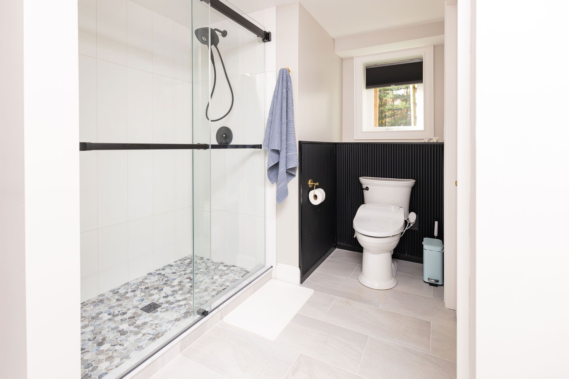 Modern bathroom with a glass shower, pebbles, and a black accent wall.