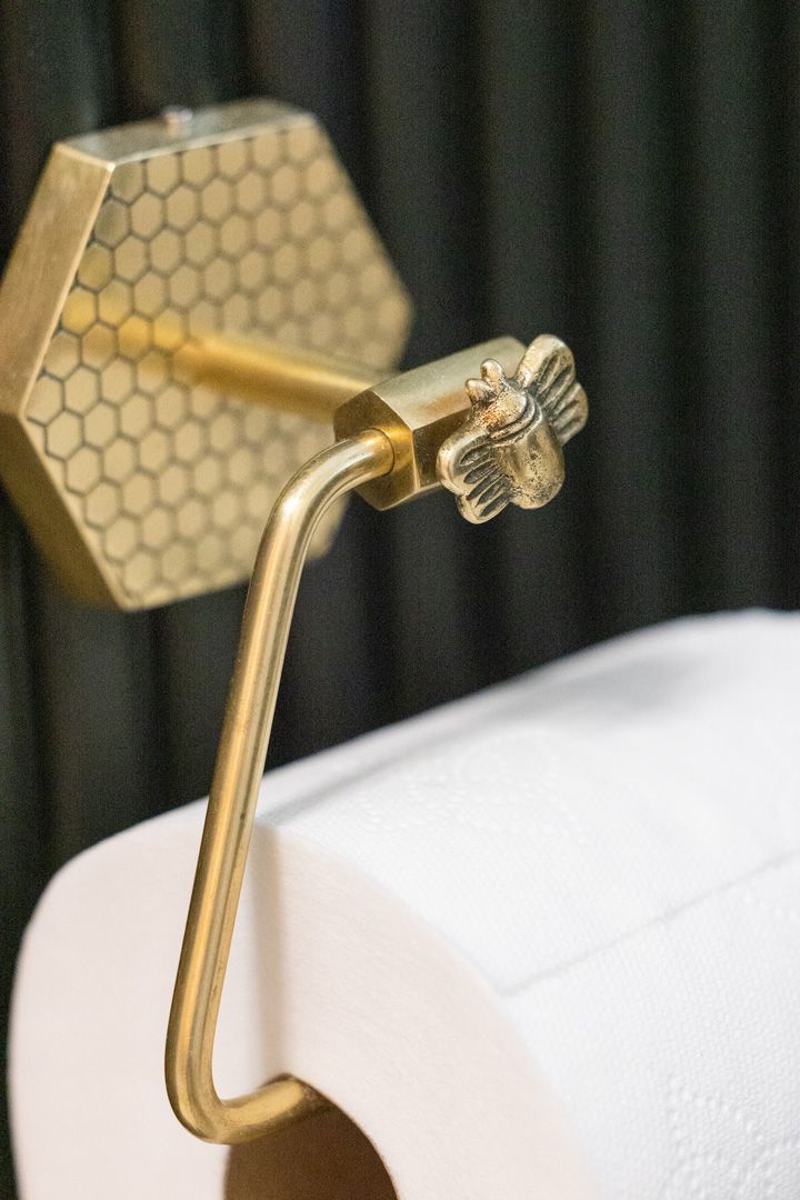 Gold toilet paper holder with honeycomb backplate, bee accent, and a roll of white toilet paper.