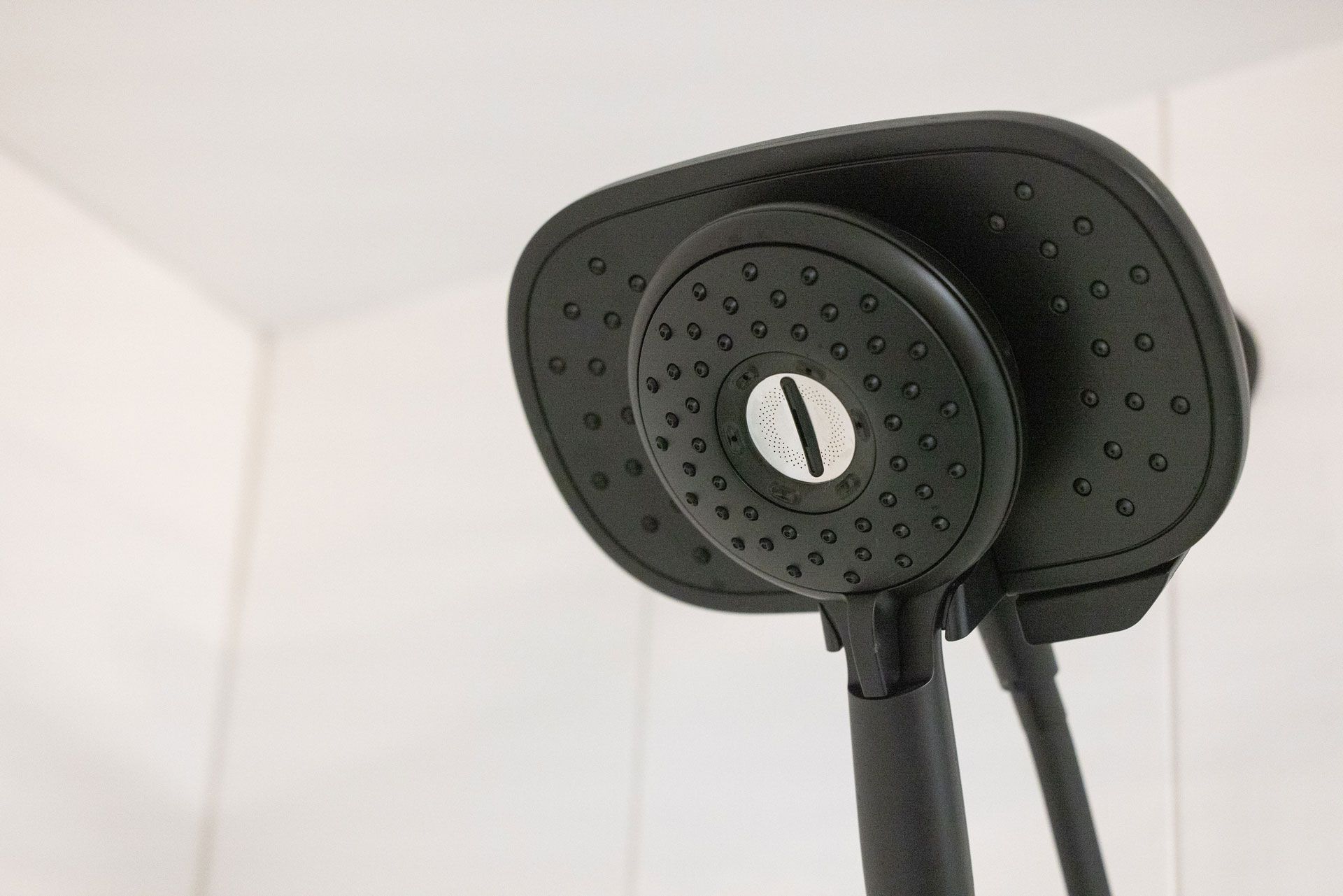 Black showerhead in a white tiled bathroom.