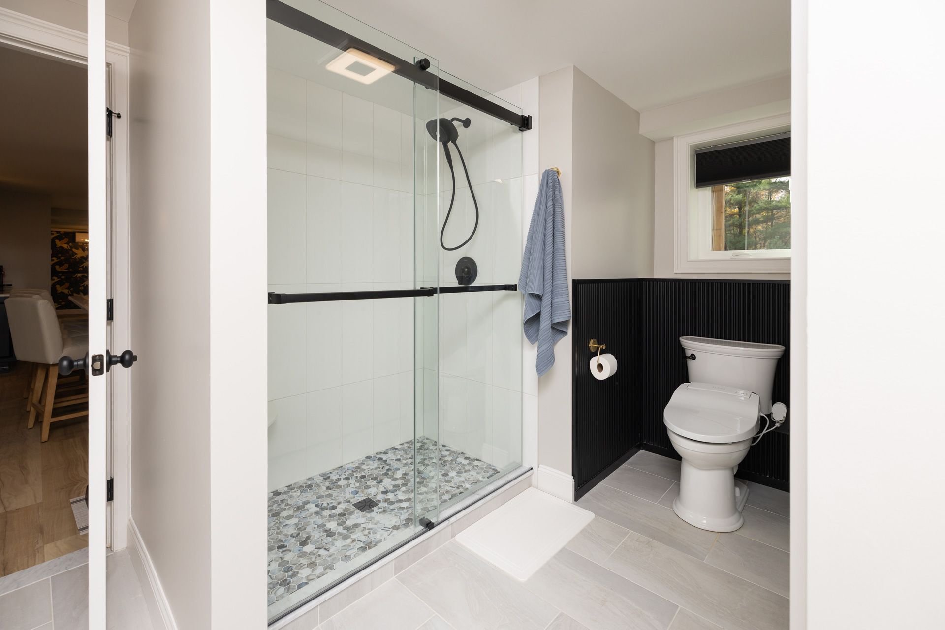 Modern bathroom with glass shower, pebble floor, white toilet, and black accent wall.